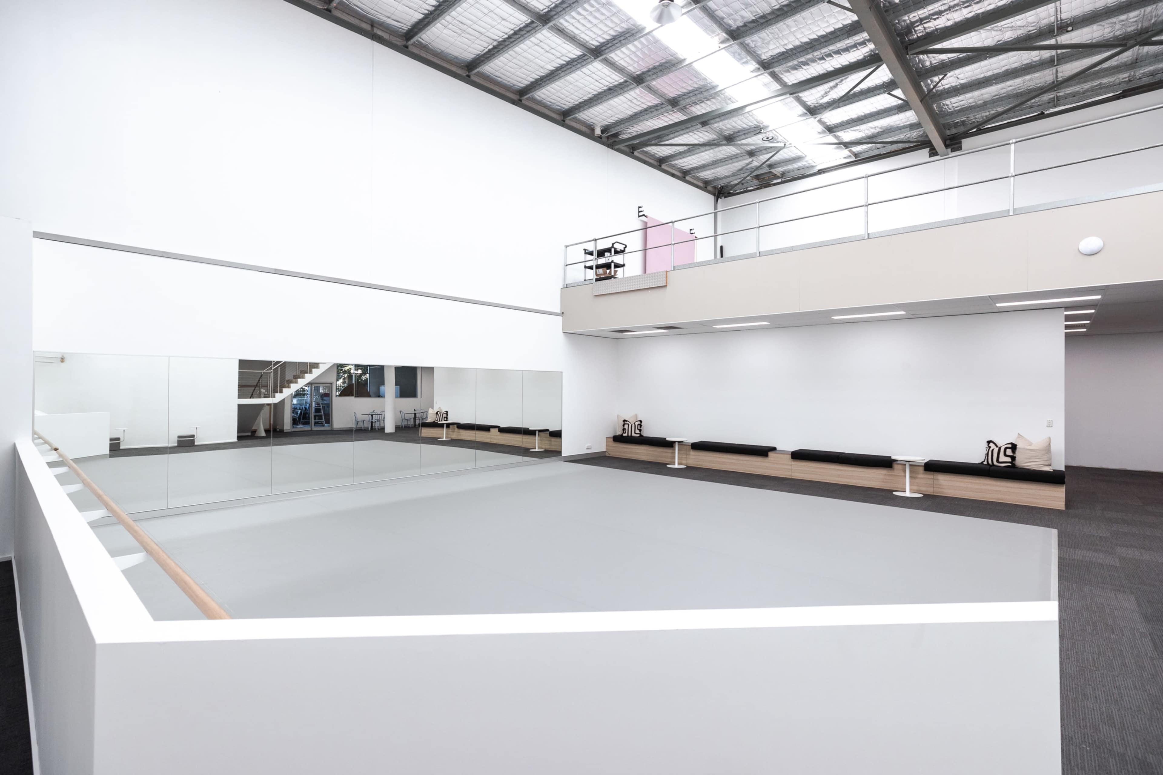 A spacious studio with a mirrored wall, a gray floor mat, and seating along the perimeter.