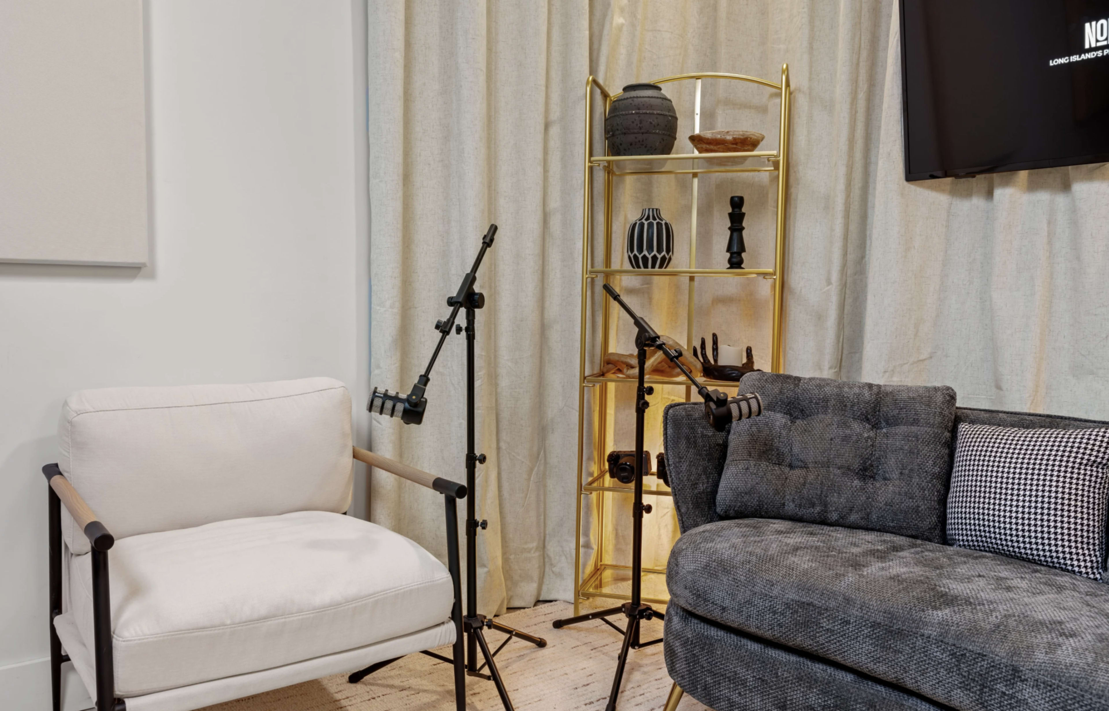 The image shows a modern living area featuring a white armchair and a dark gray couch, with a decorative shelf holding various objects in the background.