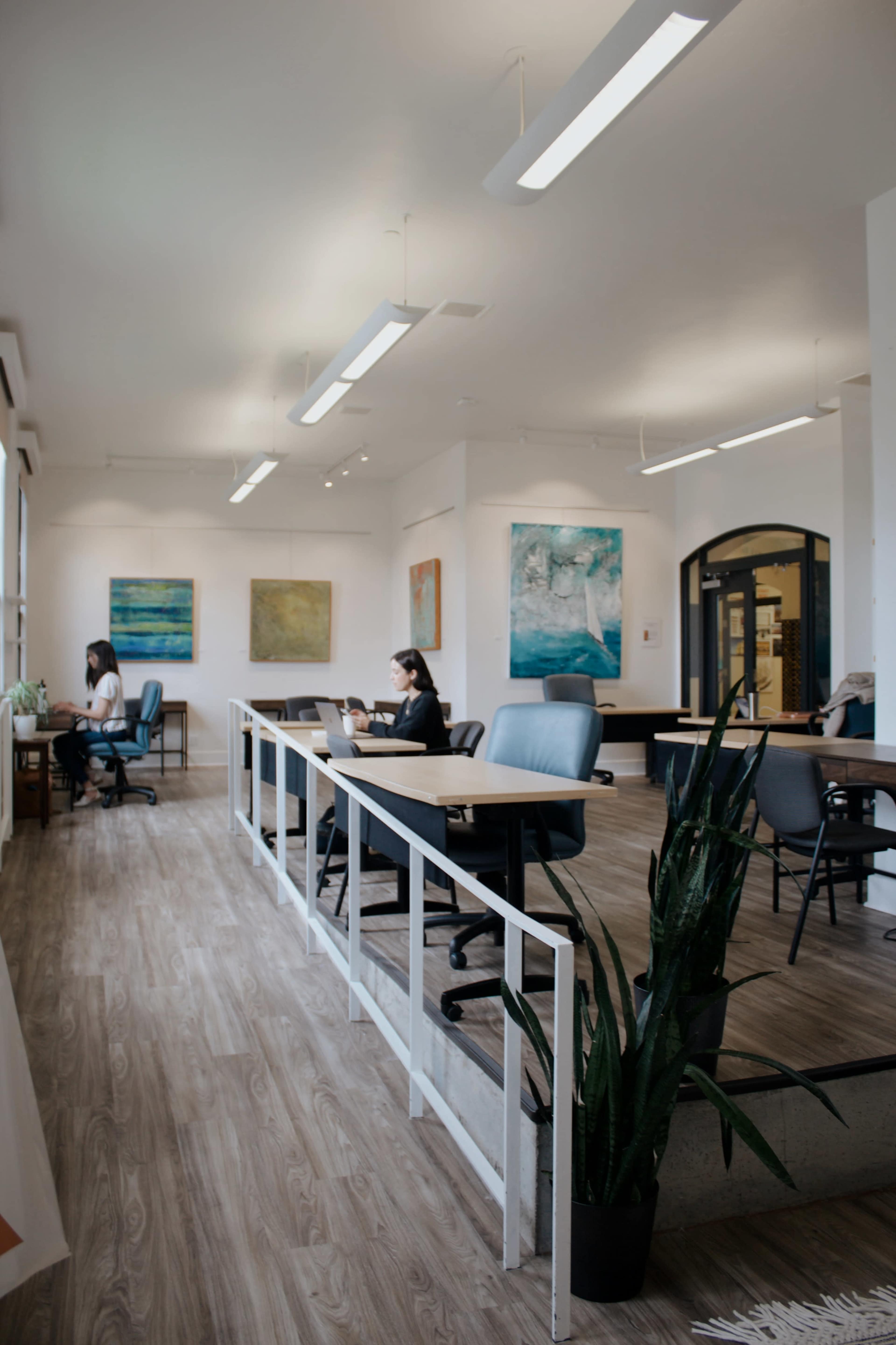 A bright, modern office space with multiple workstations, artwork on the walls, and individuals working at their desks.