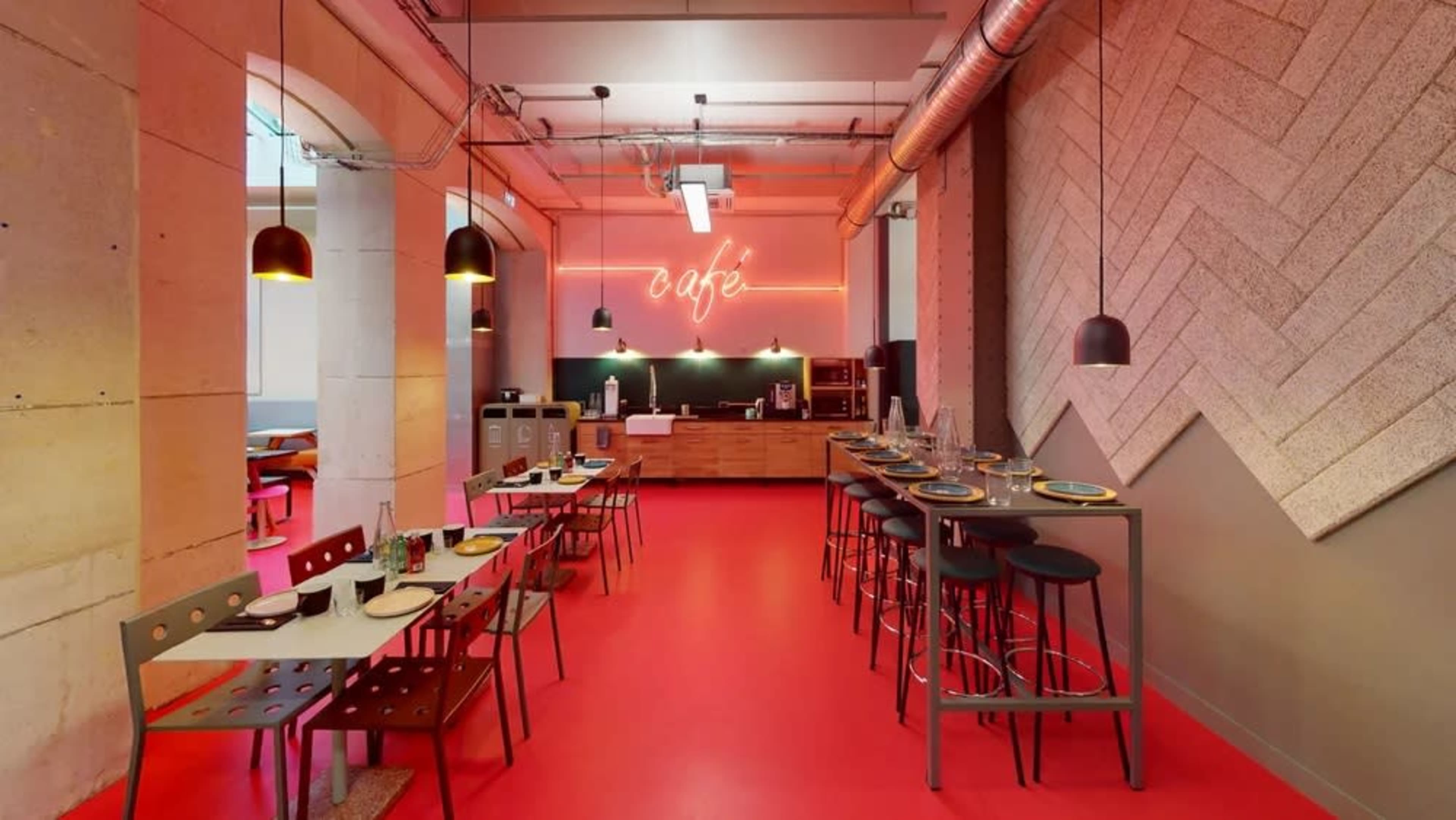 A modern café interior features red flooring, wooden furniture, and neon lights, creating distinct seating areas and a vibrant ambiance.