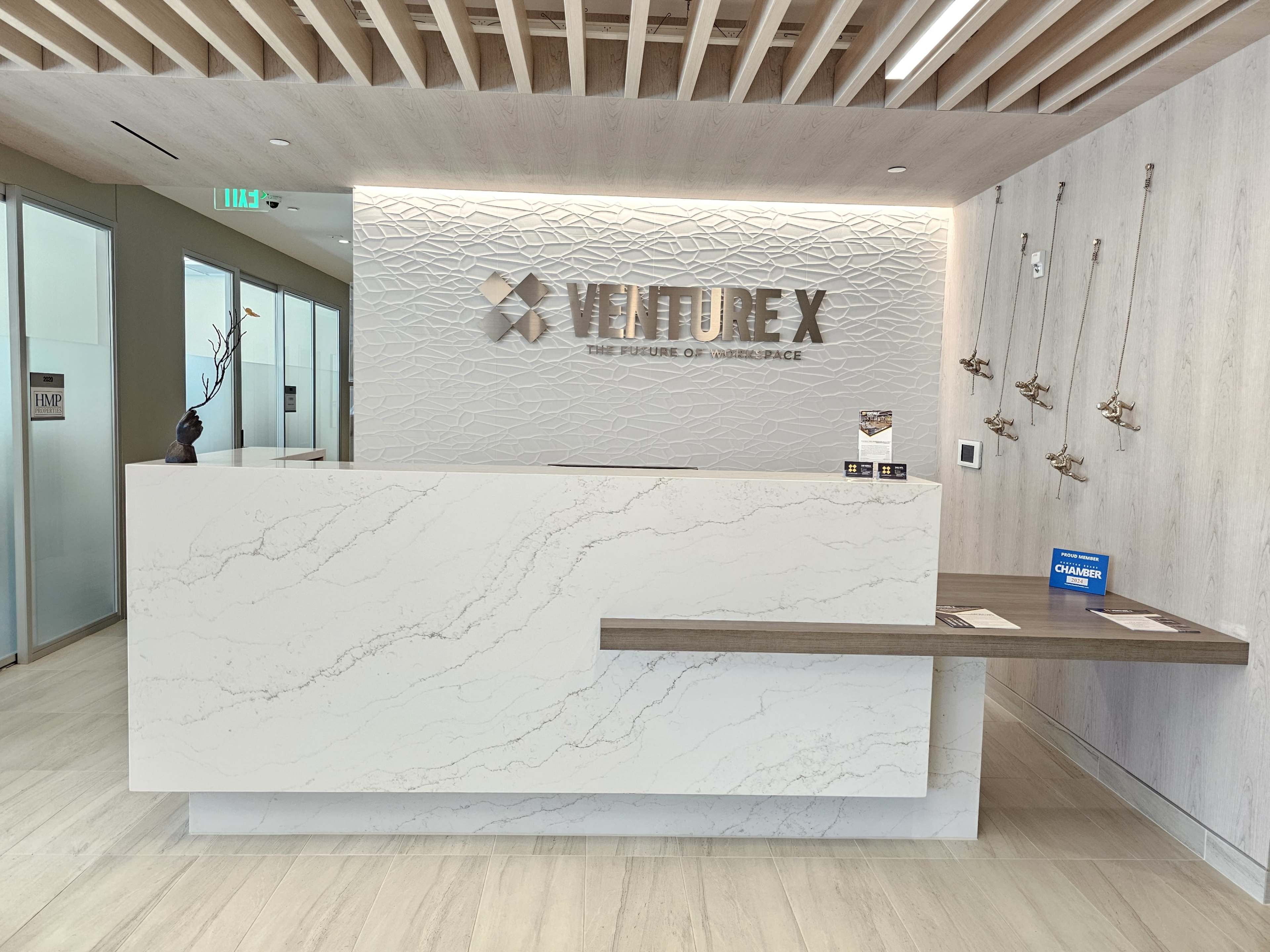 A modern reception desk with a sleek white surface and a wood accent in a well-lit office lobby featuring decorative elements on the wall.
