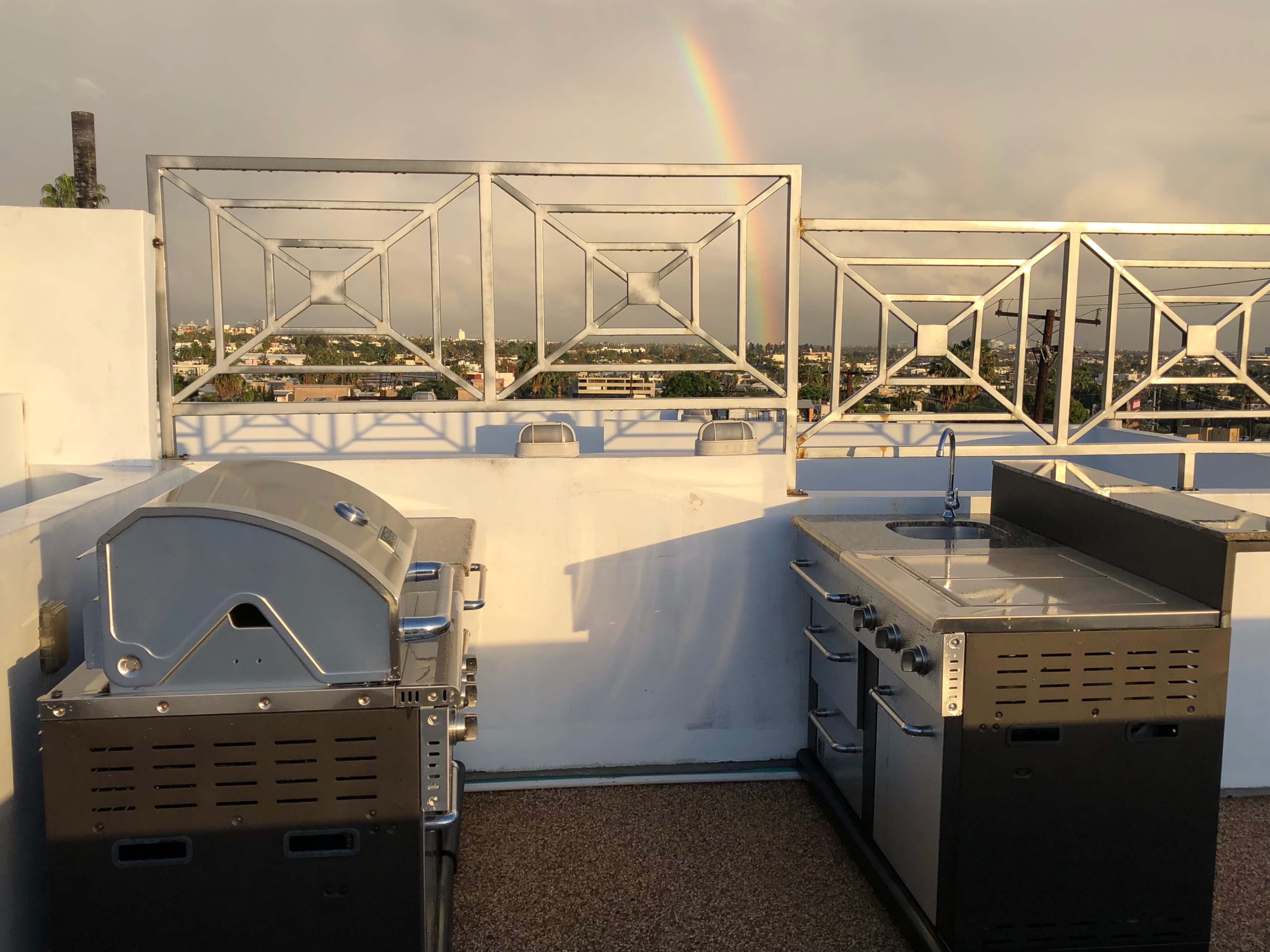 Two stainless steel grills and a cooking station on a rooftop with a rainbow in the background.