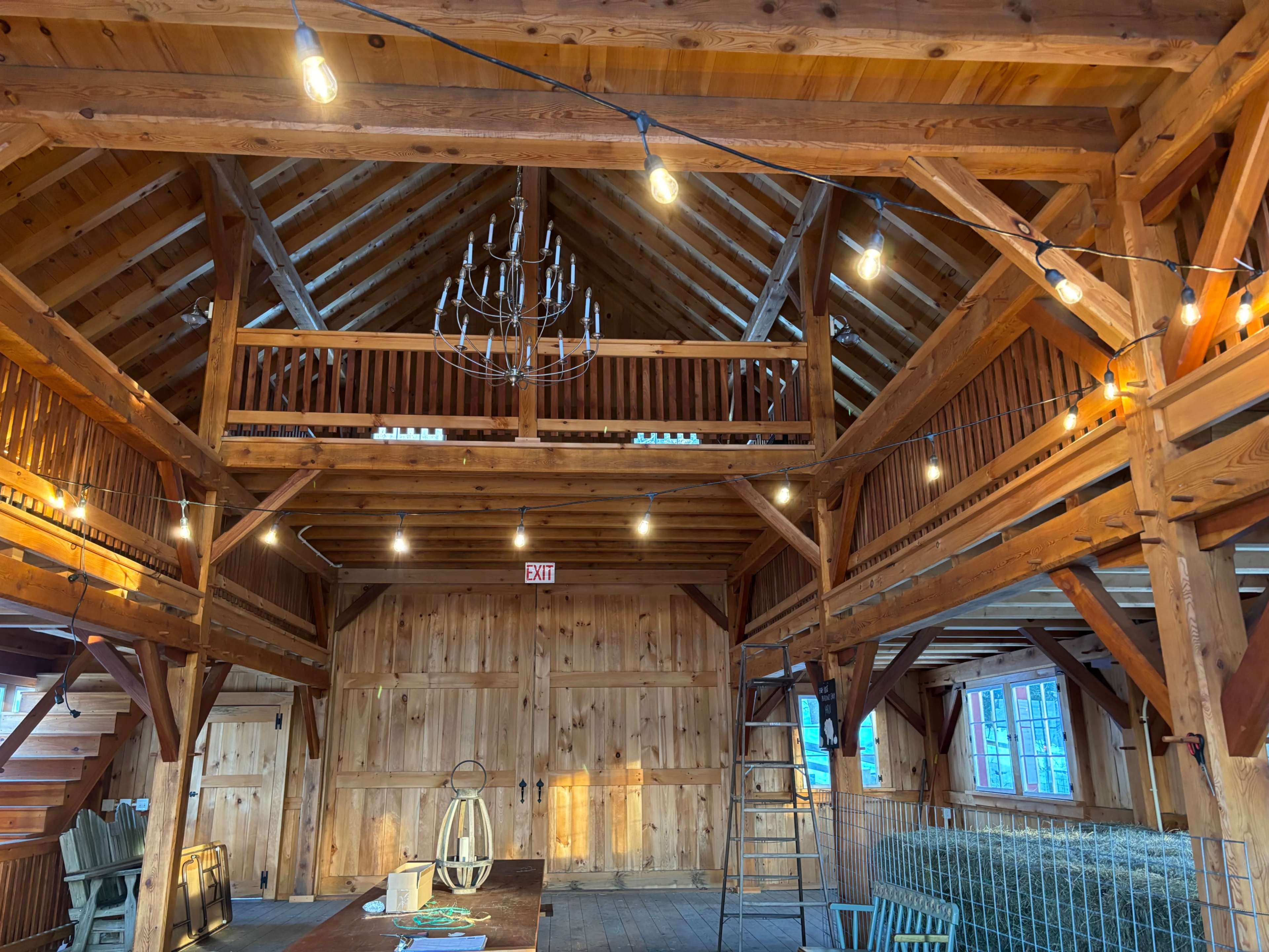 The interior of a wooden barn featuring a loft, exposed beams, and decorative lighting elements.