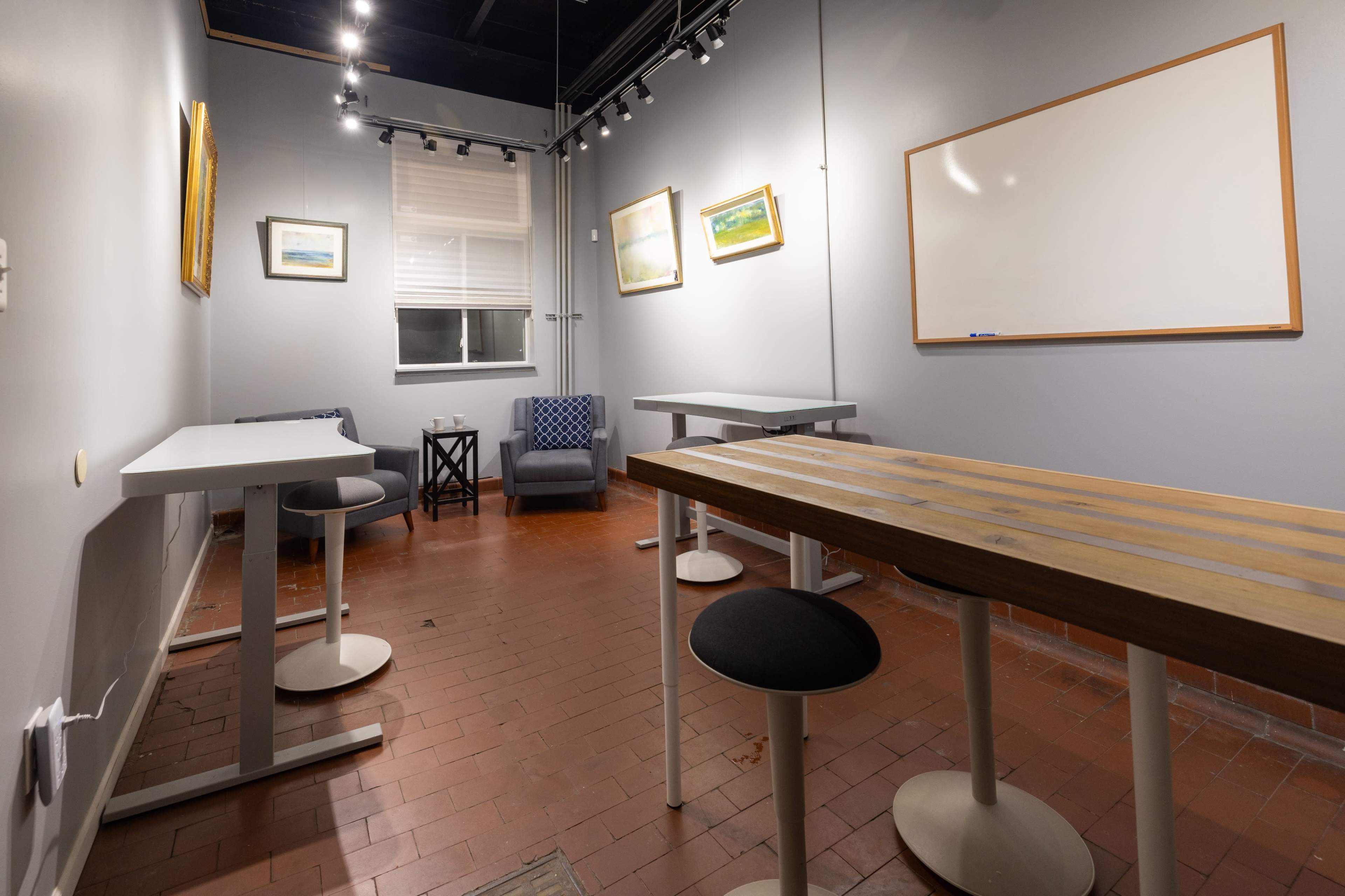 A small, minimally furnished meeting room with two tables, a chair, and wall-mounted artwork.