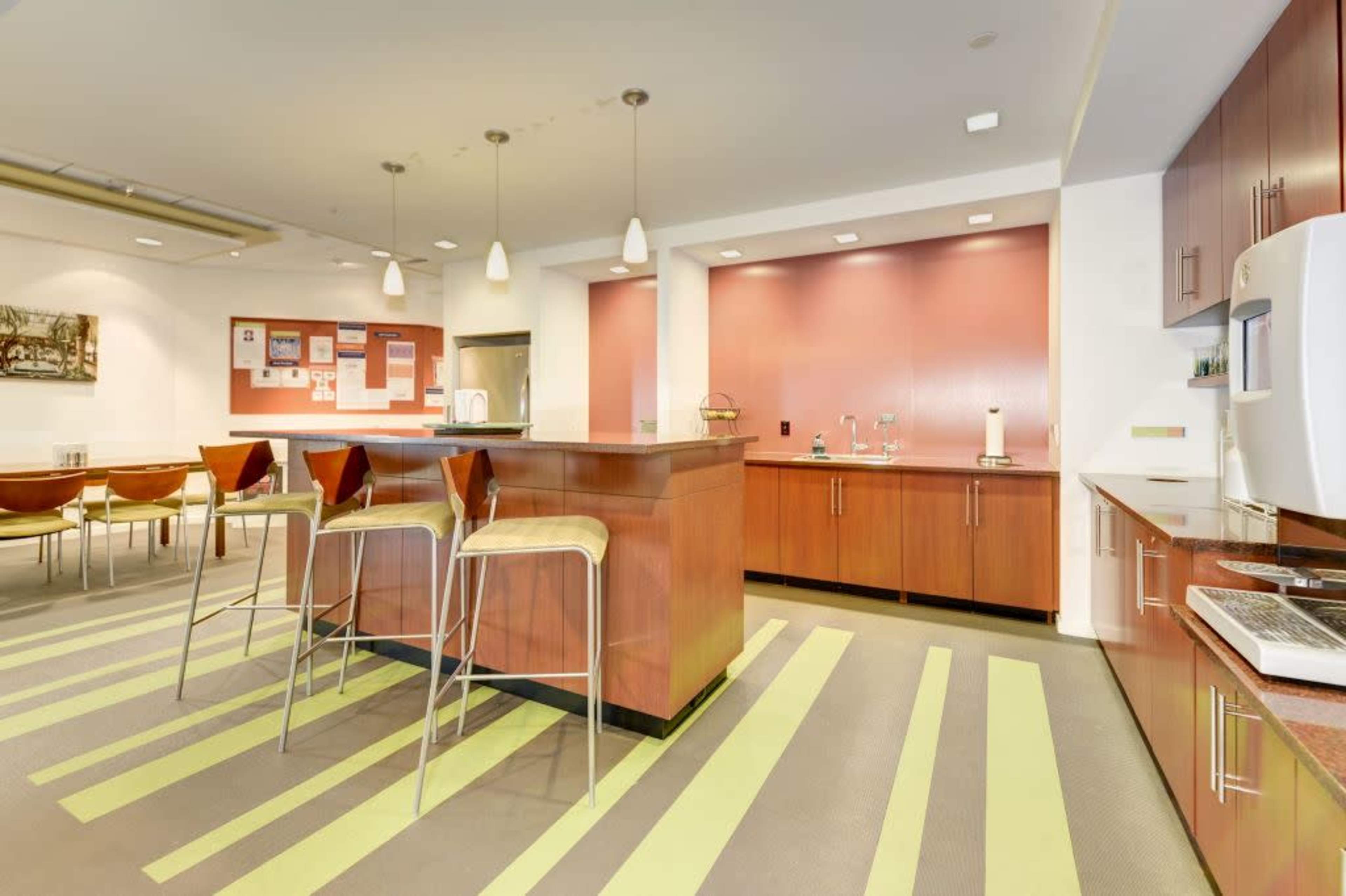 A modern kitchen area features a central island with bar stools, light-colored cabinetry, and striped flooring with green accents.