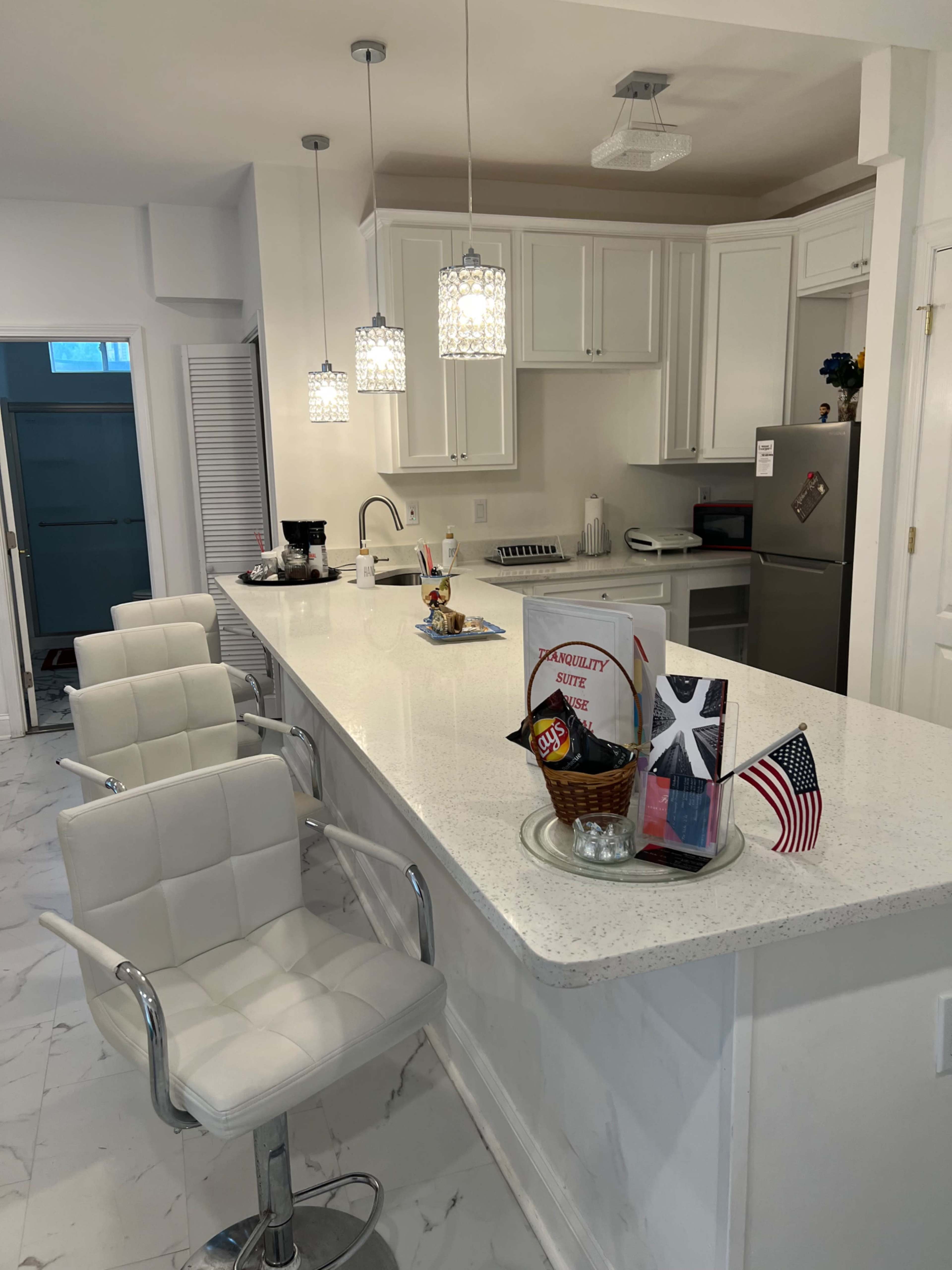 The image shows a modern kitchen with white cabinetry, a large island featuring three white bar stools, and pendant lighting above.