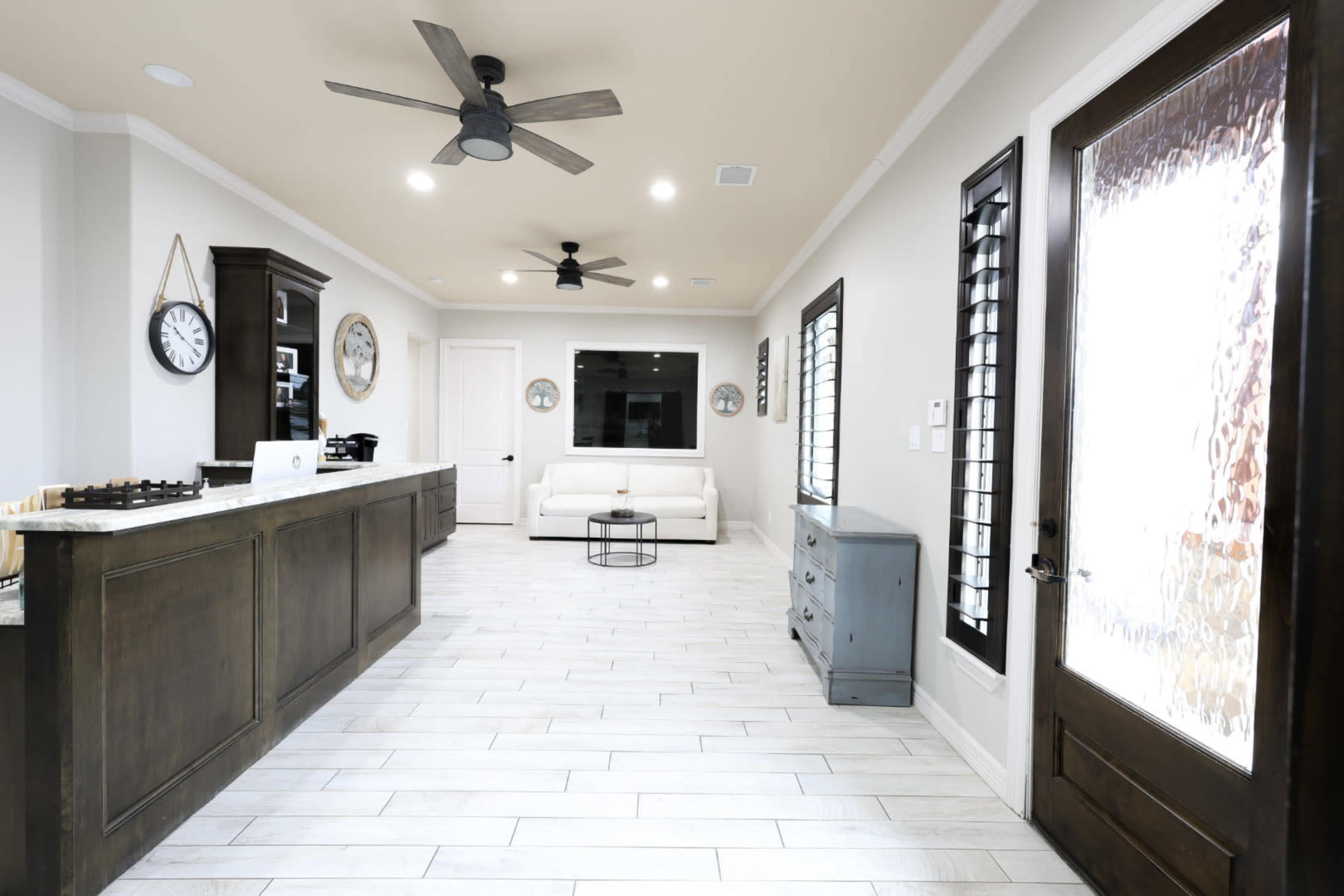 A modern kitchen and living area features a white sofa, dark wood cabinetry, and a door with frosted glass.