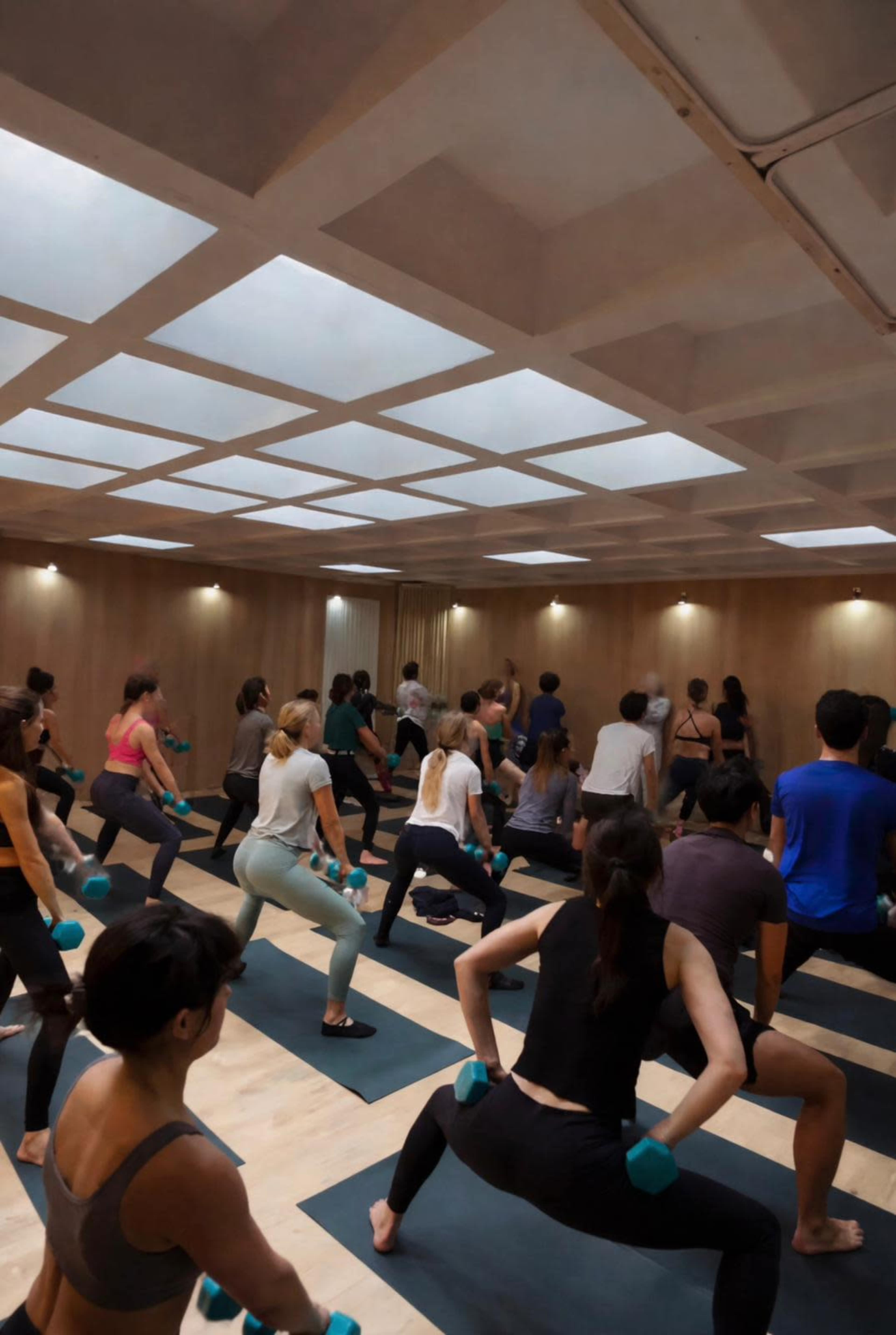 A large group of people is participating in a workout class with dumbbells in a well-lit studio.