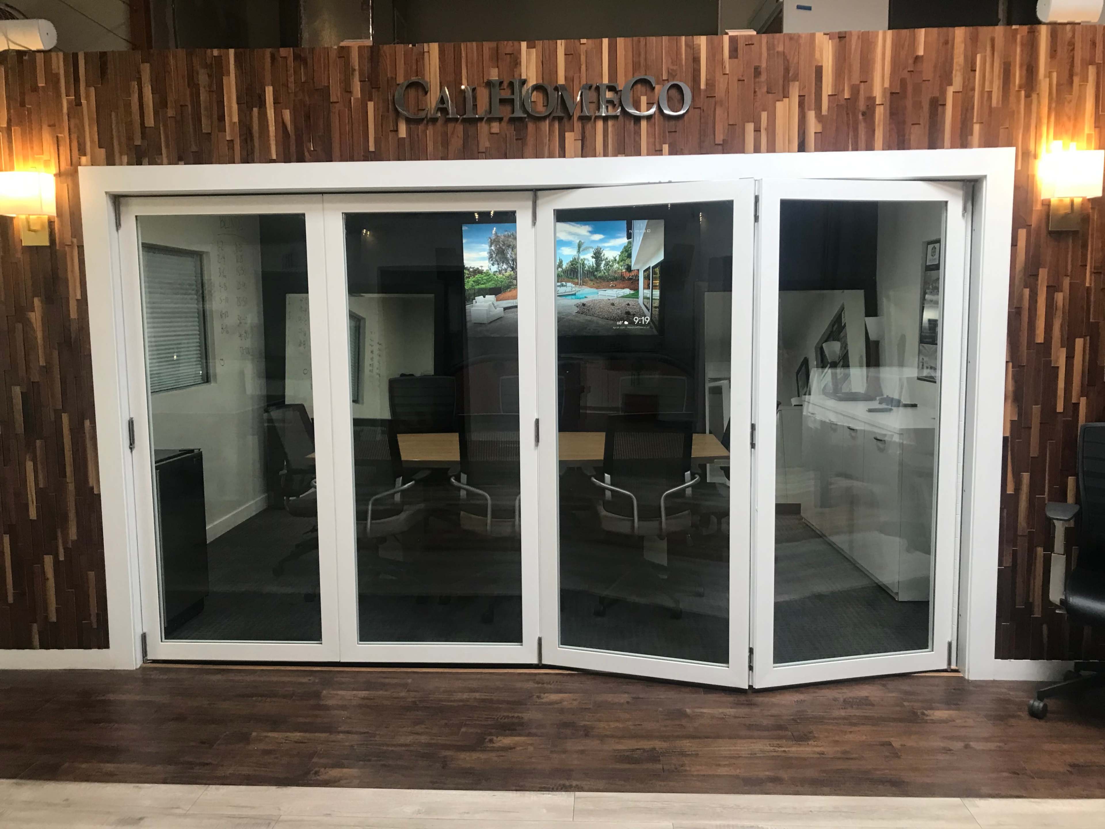 The image shows a modern office space with a glass door entry labeled "CallHomeCo," surrounded by wooden paneling and featuring two desks inside.