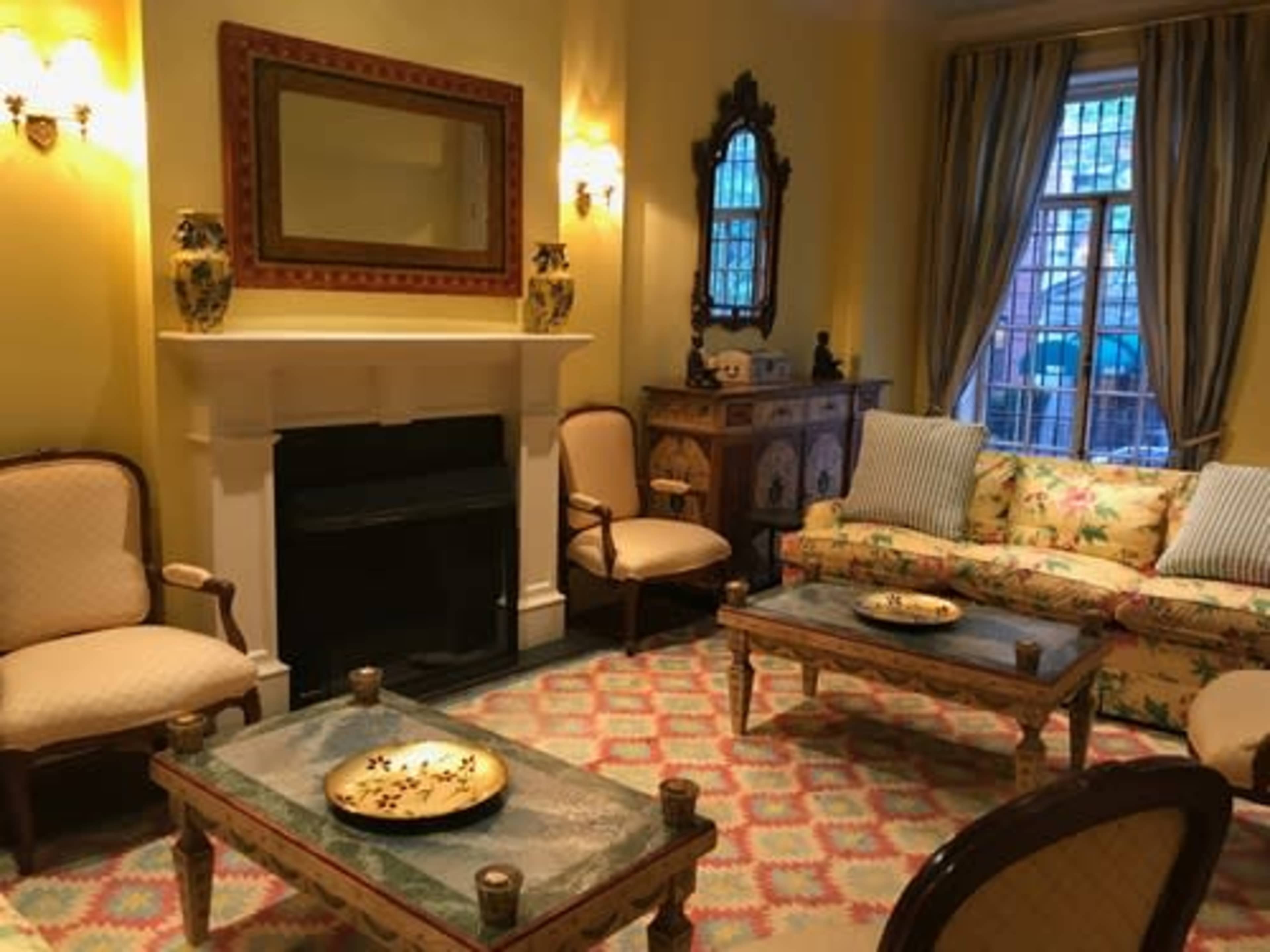 A cozy living room with a floral-patterned sofa, upholstered chairs, a fireplace, and decorative lighting.