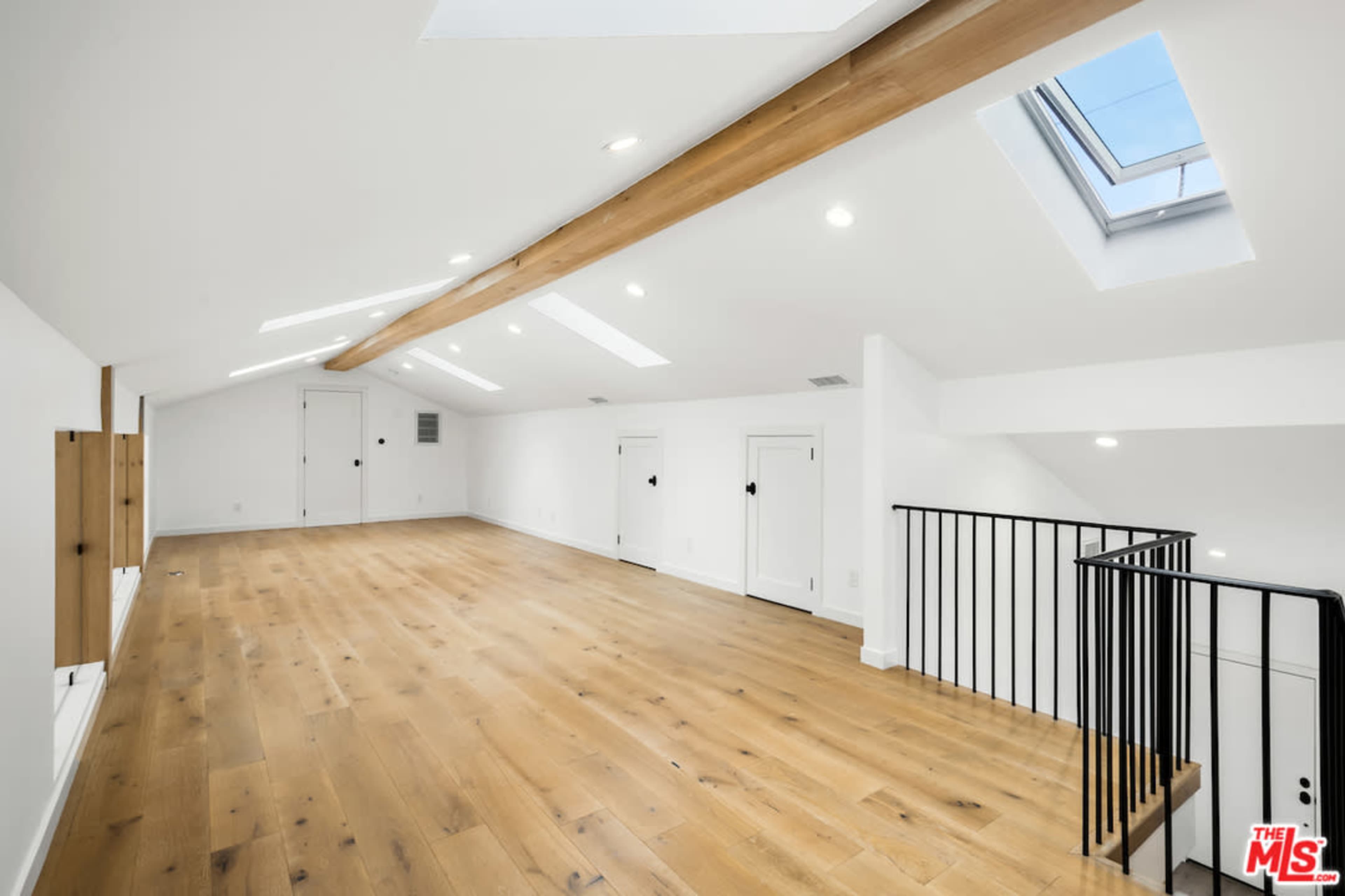 An airy, unoccupied loft space features wooden beams, skylights, and a staircase with a black railing.