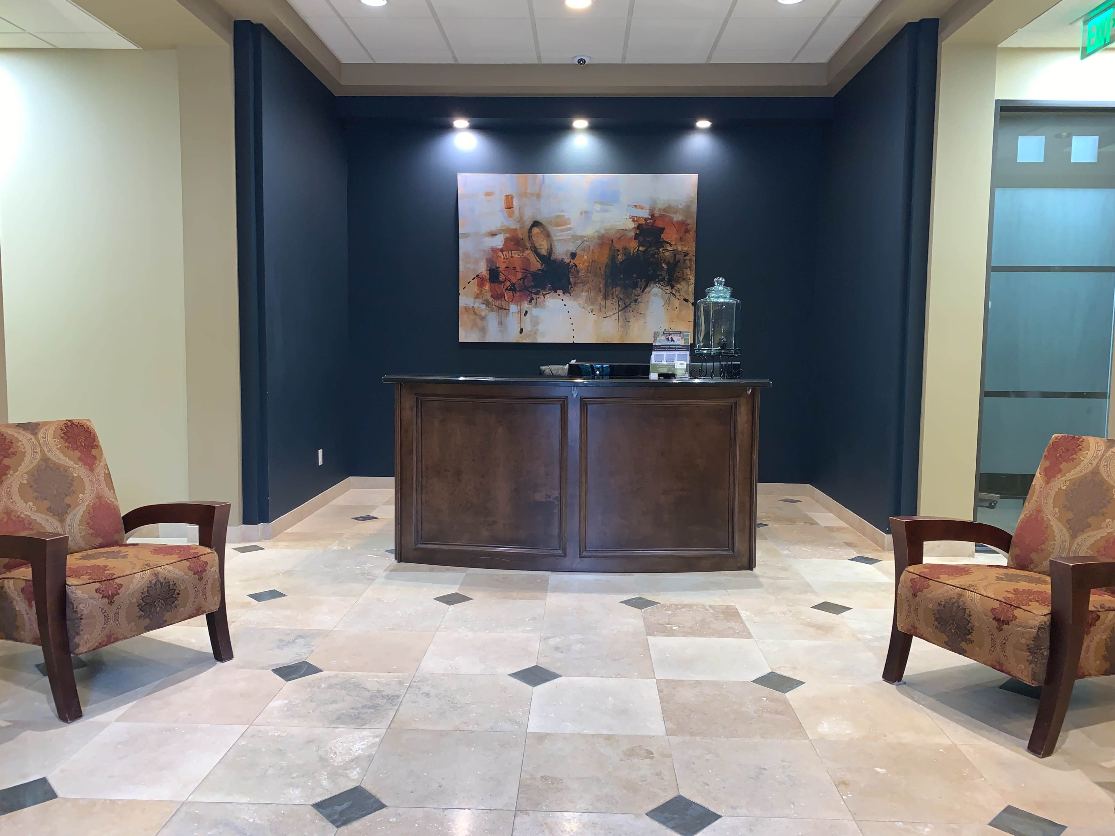 A reception area featuring a wooden front desk, two upholstered chairs, and a large abstract painting on the wall.