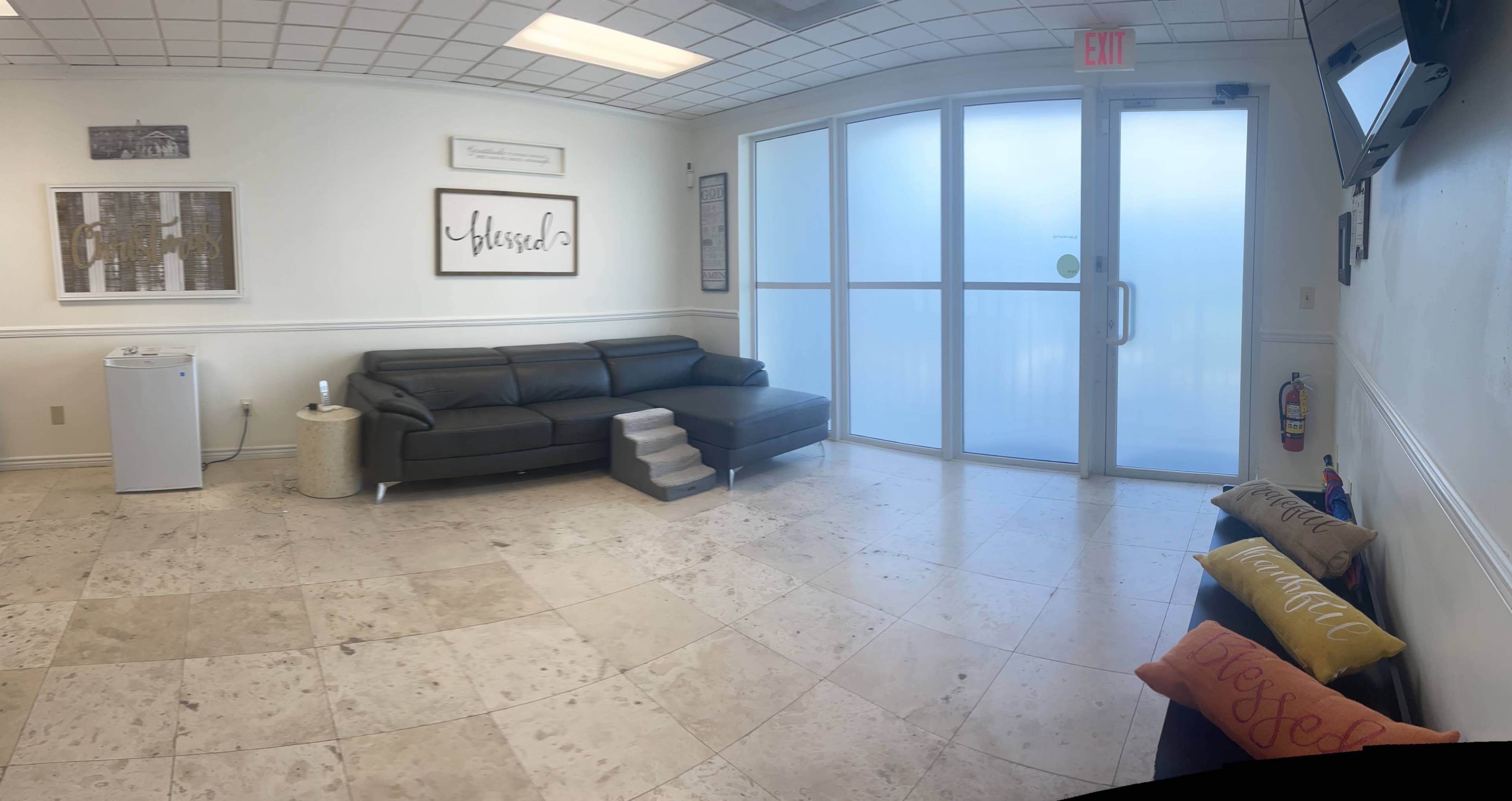 A bright waiting area with a black sofa, a small set of stairs, a television mounted on the wall, and decorative pillows on a bench.