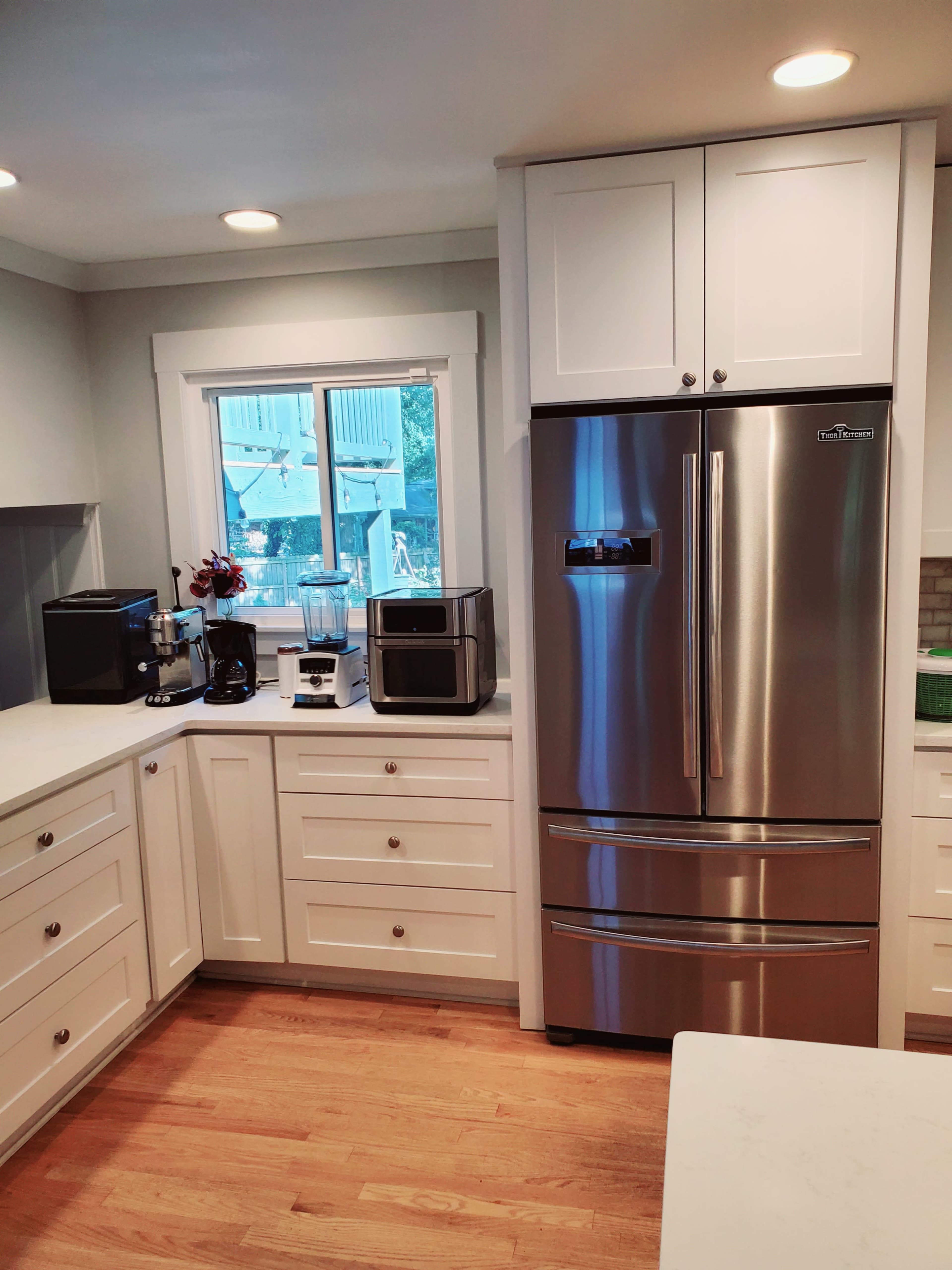 A modern kitchen with white cabinetry, a stainless steel refrigerator, and various kitchen appliances on the countertop.