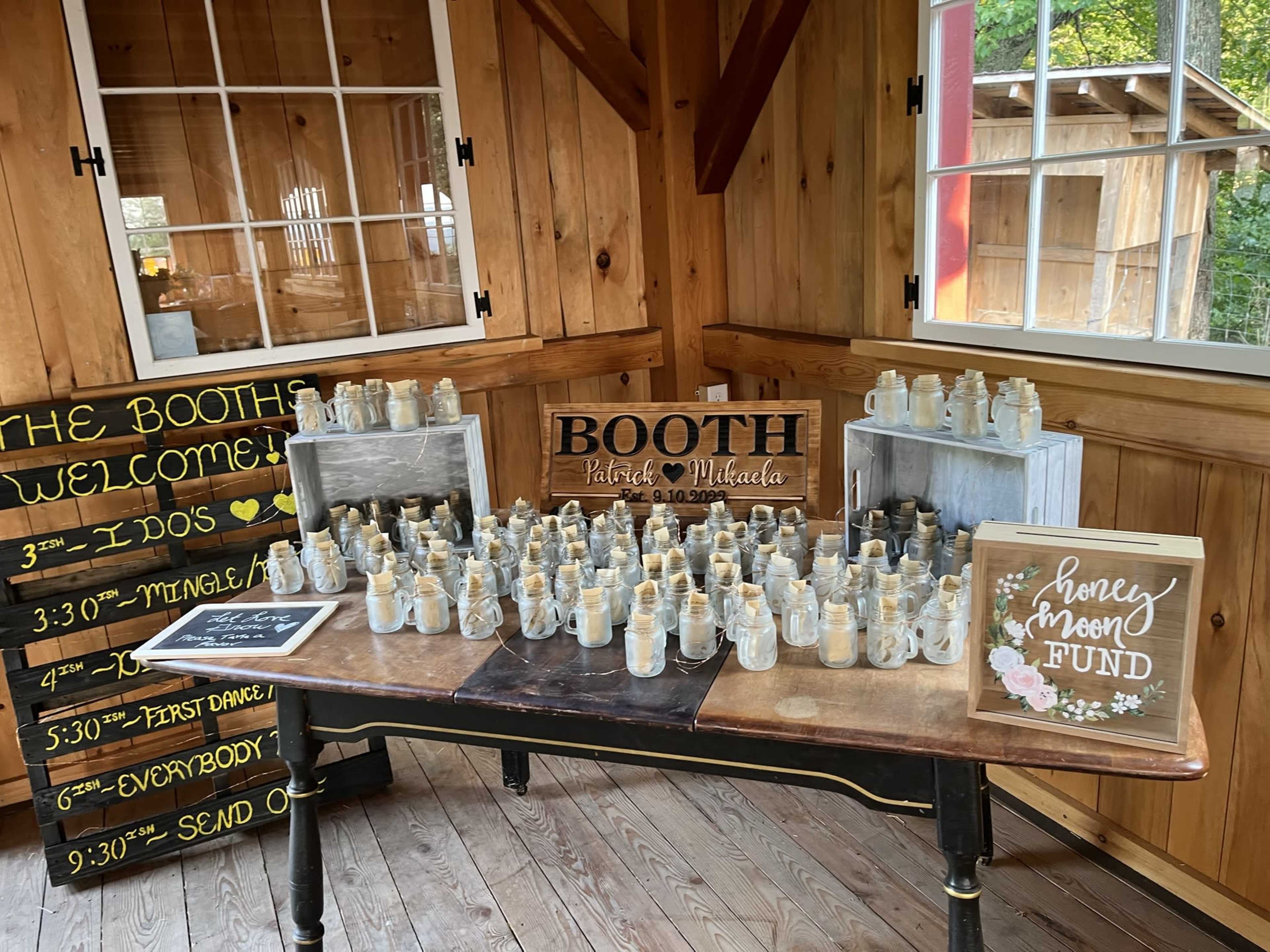 A wooden table displays numerous small jars, alongside a sign that reads "BOOTH," and additional decorations, all set within a rustic interior.