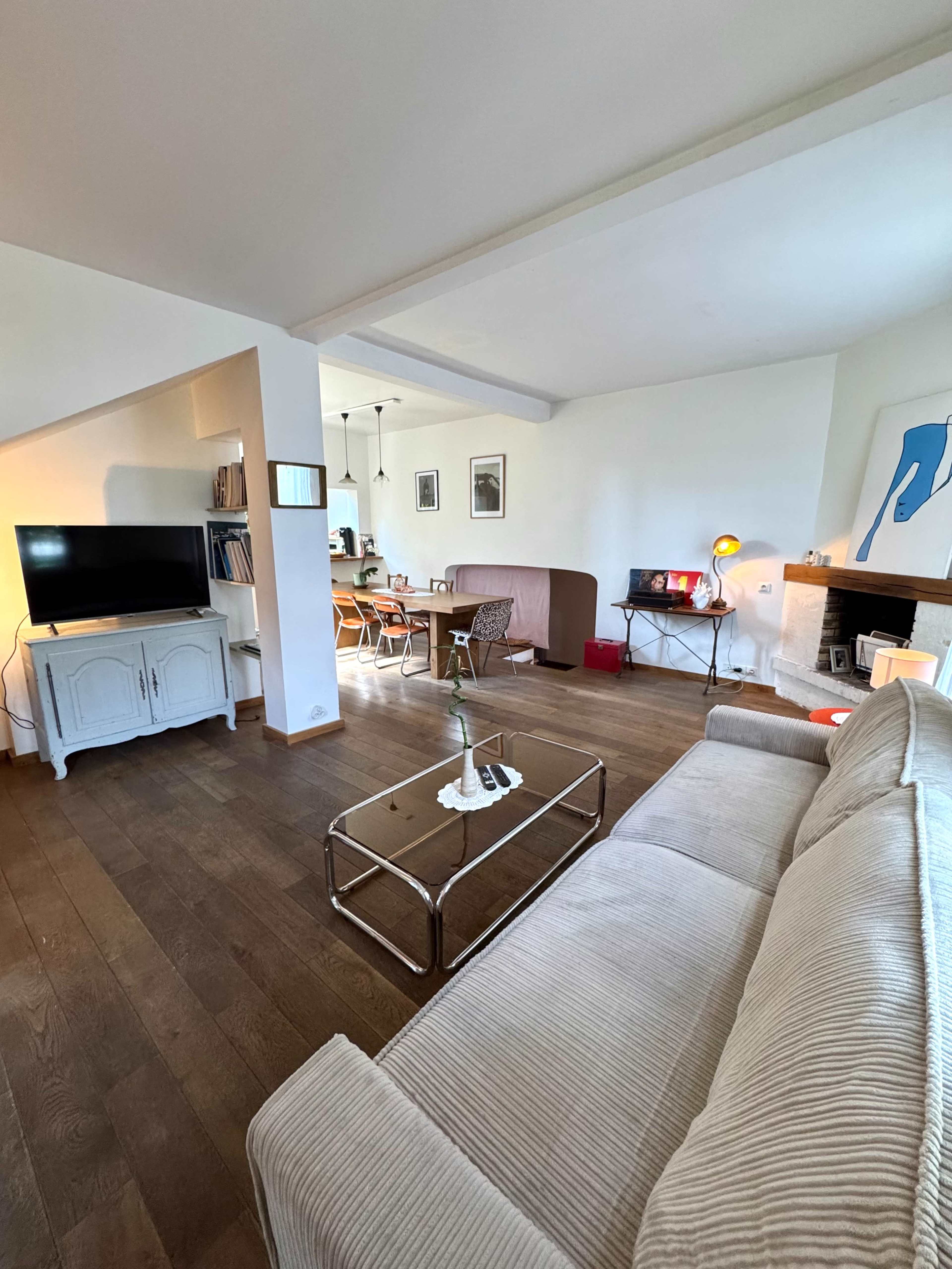 The image shows a bright living room featuring a sofa, a coffee table, a television, and an adjacent dining area with a modern design.