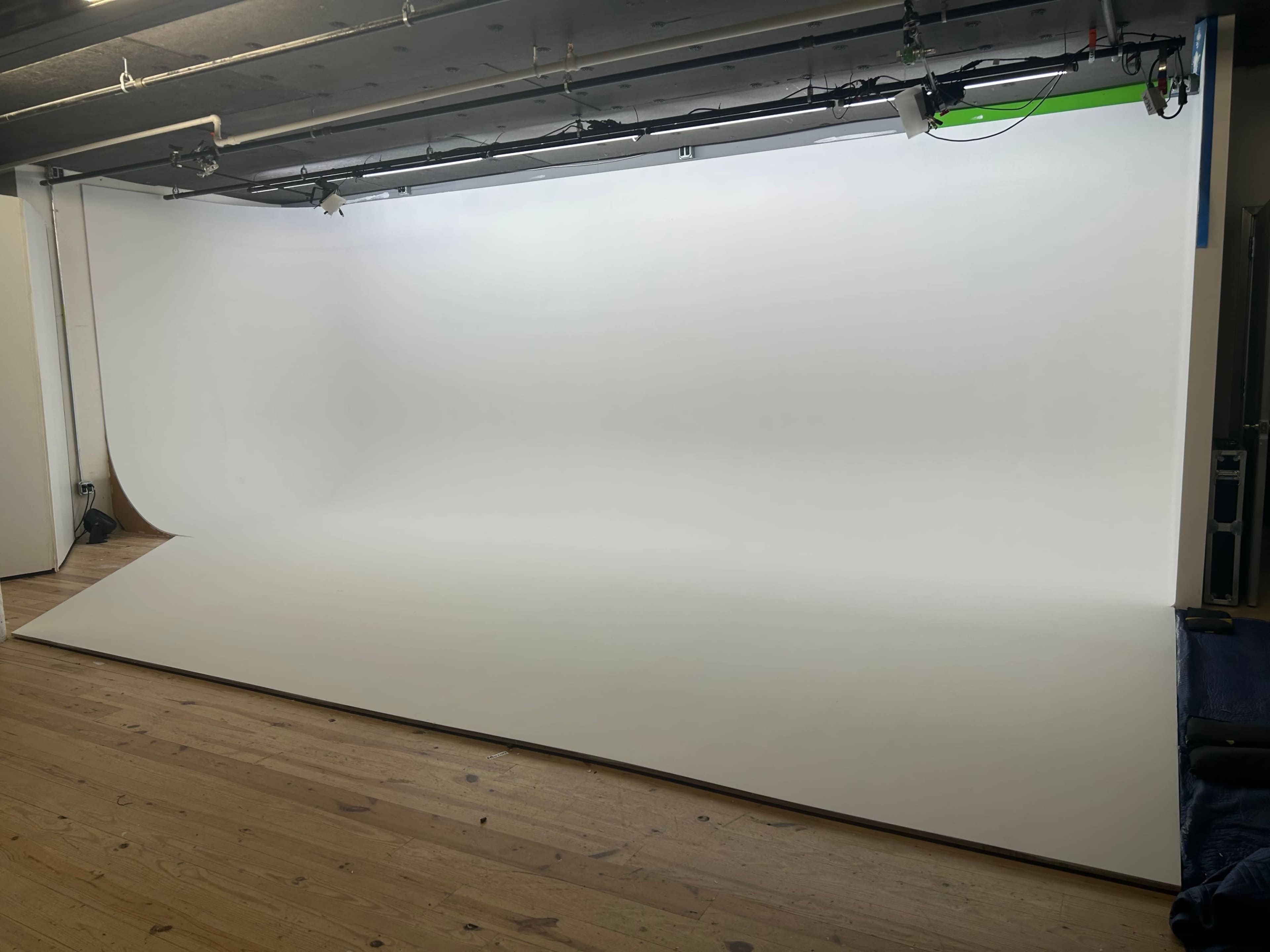 The image shows a spacious studio with a seamless white backdrop and wooden flooring.