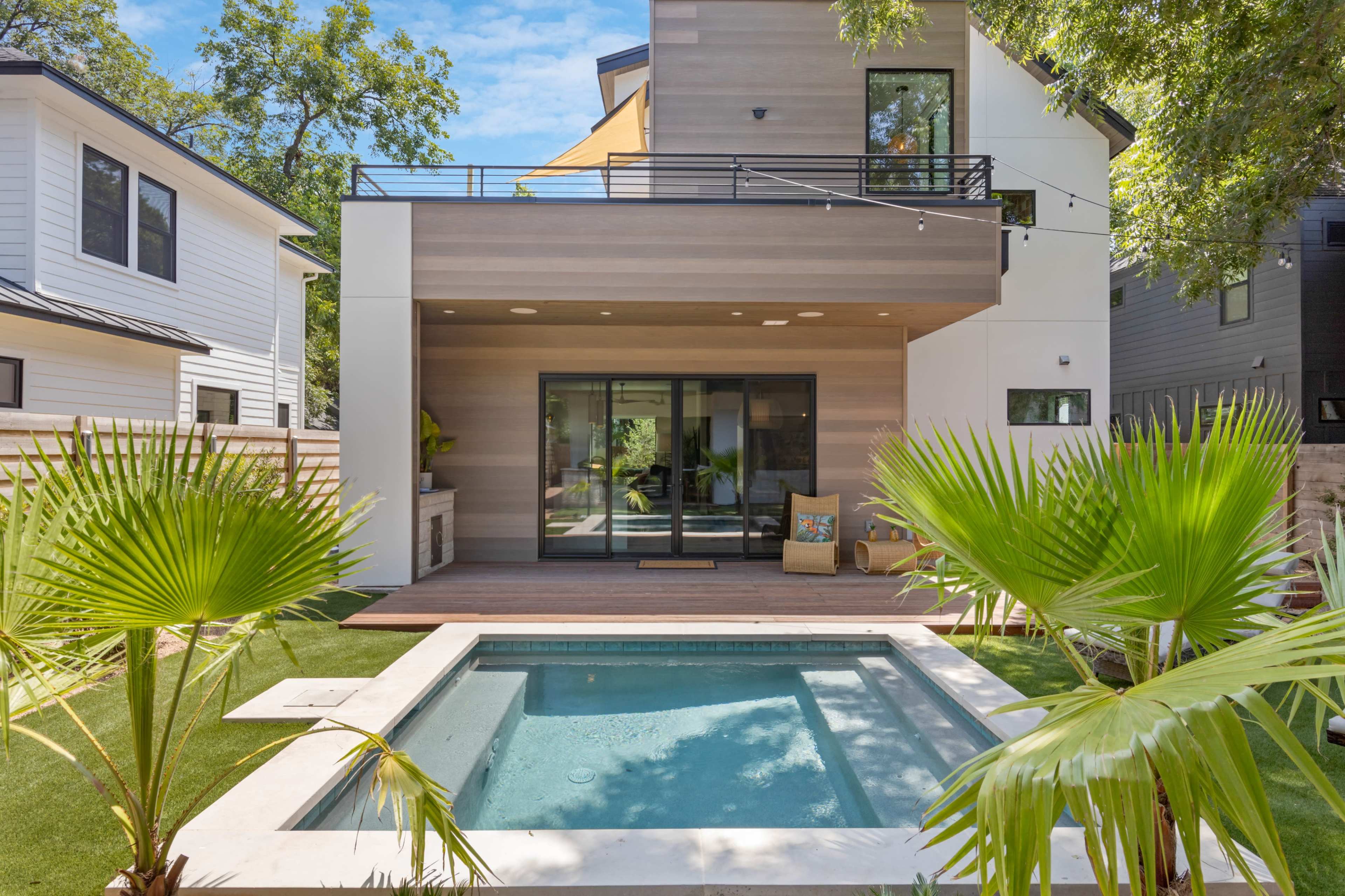 The image shows a modern home with a small pool surrounded by palm plants and a wooden deck.