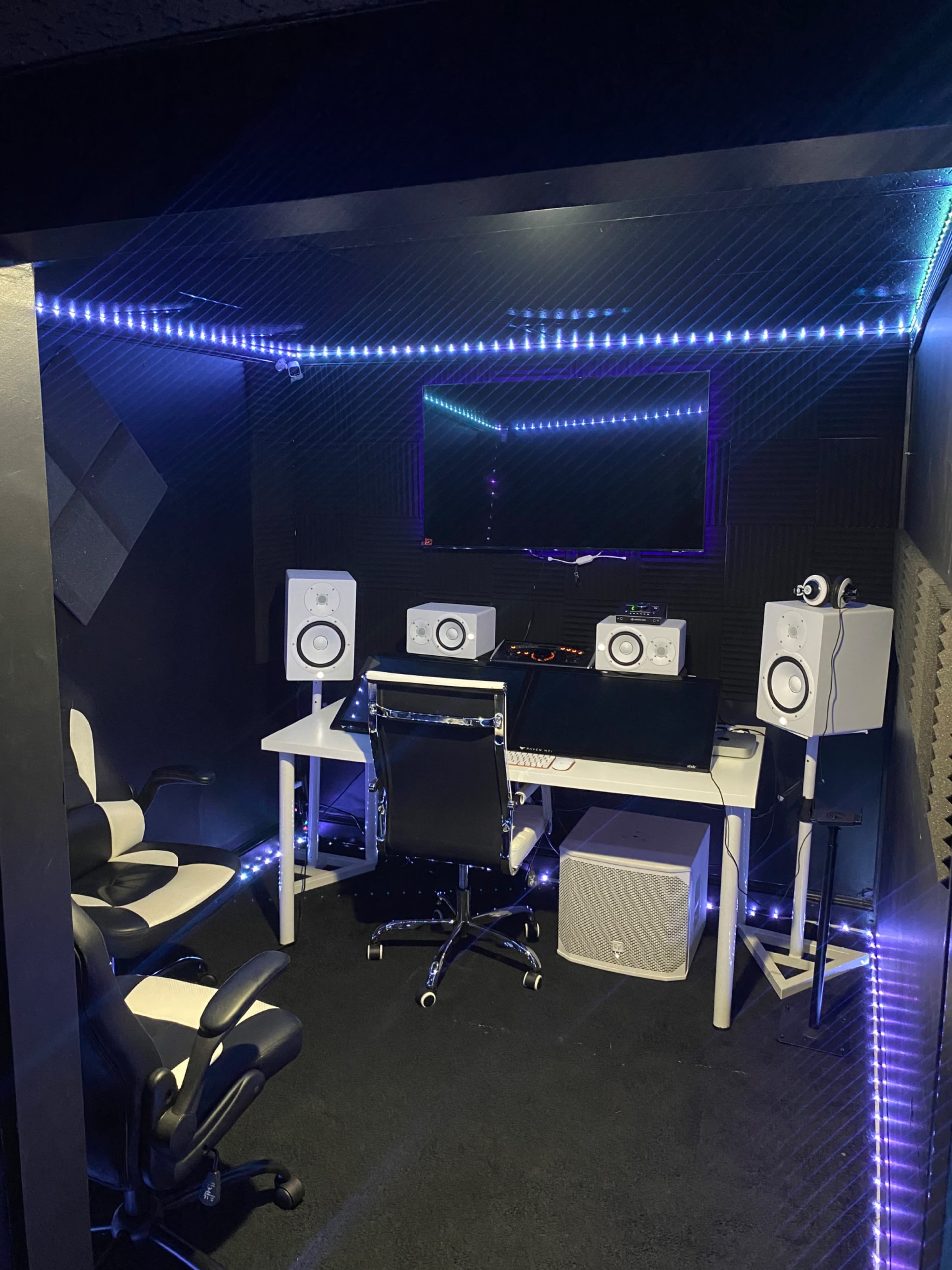 A modern music studio equipped with speakers, a desk, and ambient lighting.