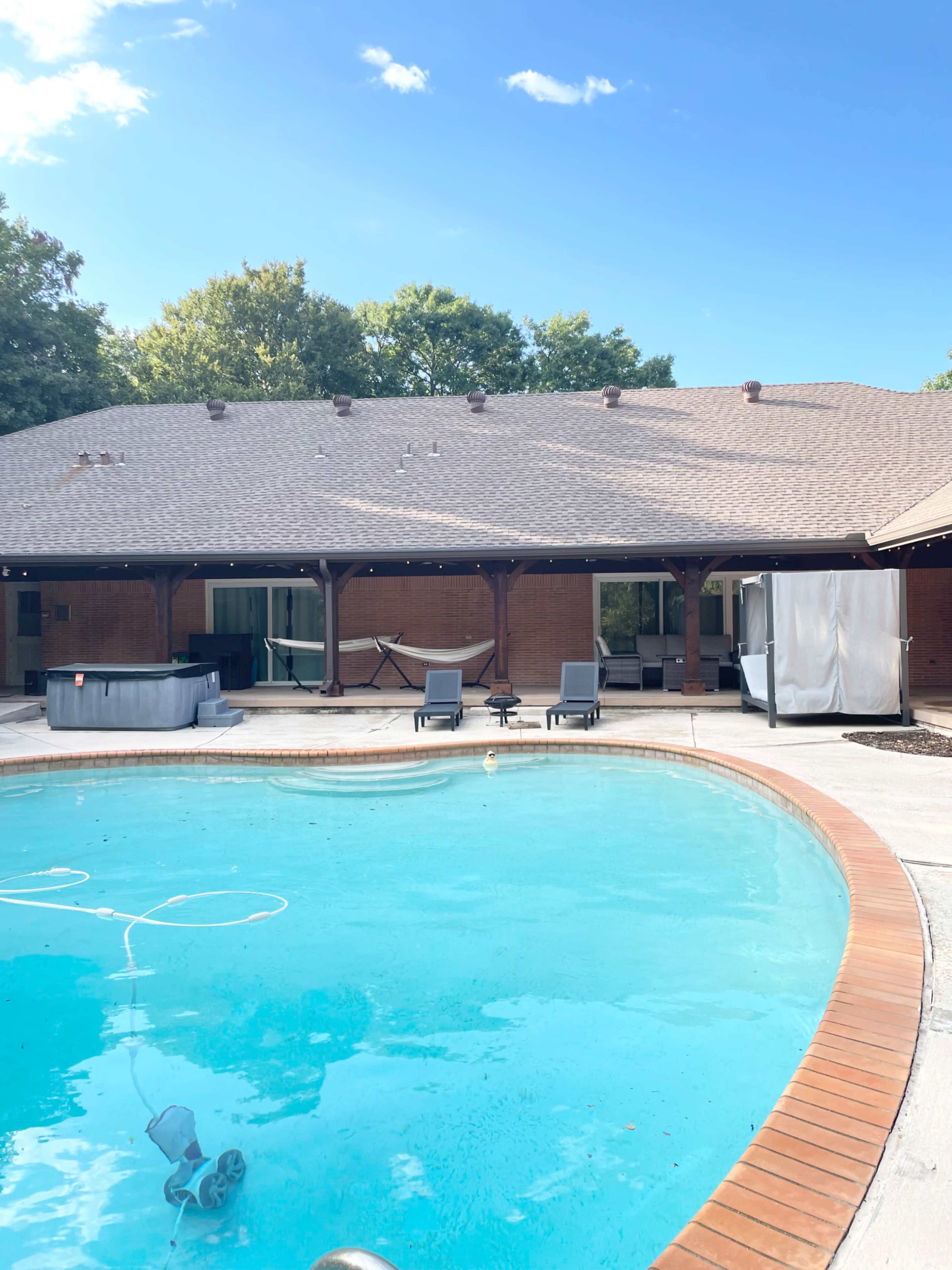 The image shows a residential backyard with a swimming pool, patio furniture, and a house with a shingled roof in the background.