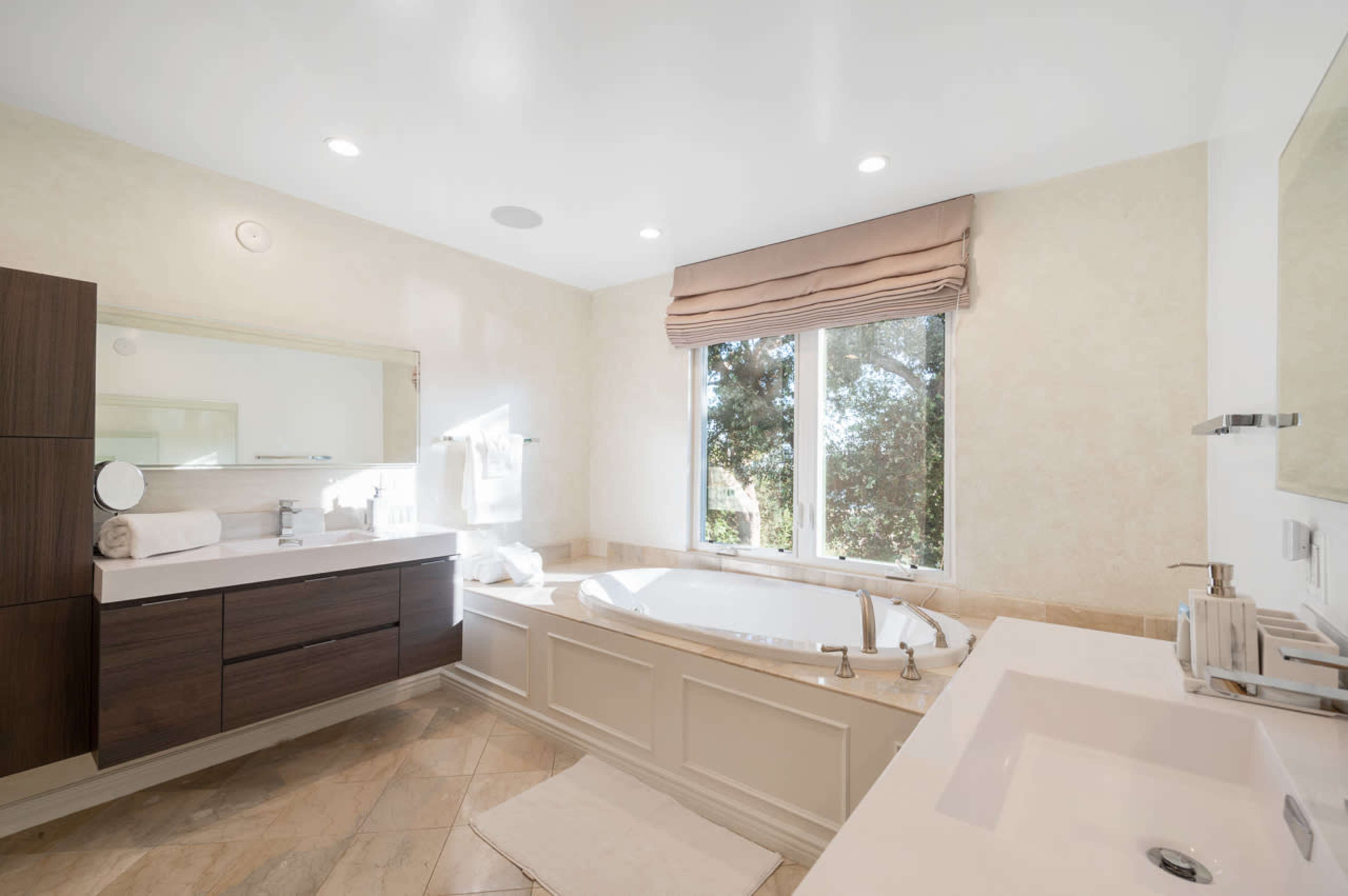 A modern bathroom featuring a large bathtub, double sink vanity, and a window with natural light coming in.