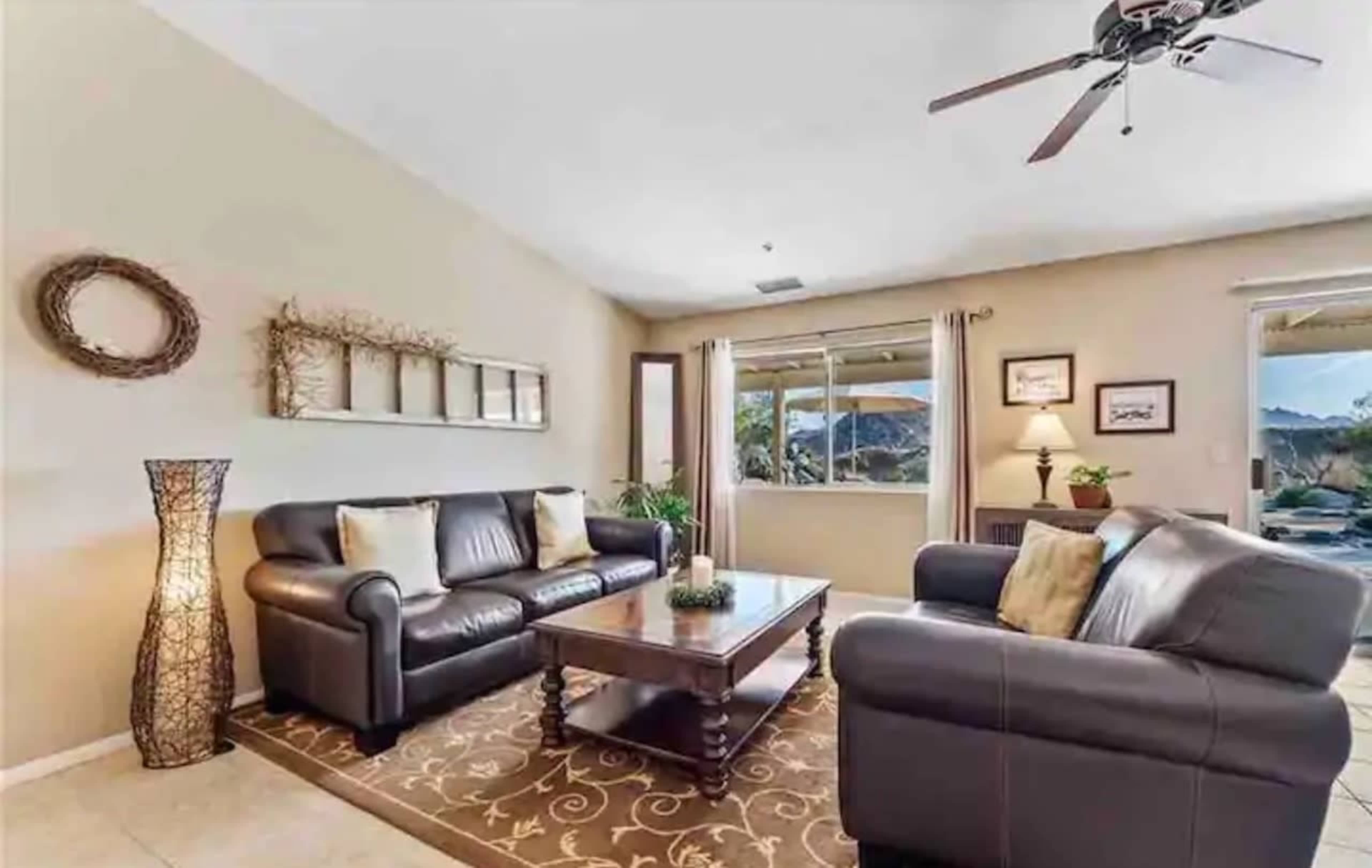 A living room with two leather sofas, a wooden coffee table, and a decorative floor lamp, with a view of the outdoors visible through a window.