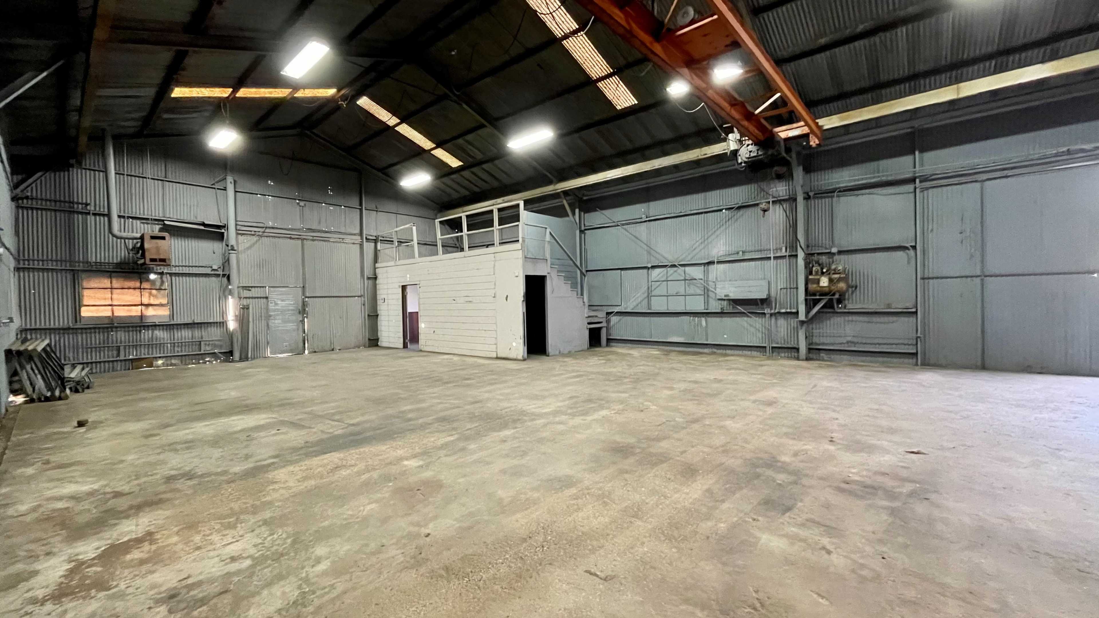 An empty industrial warehouse with a high ceiling, metal walls, and a loft area on one side.
