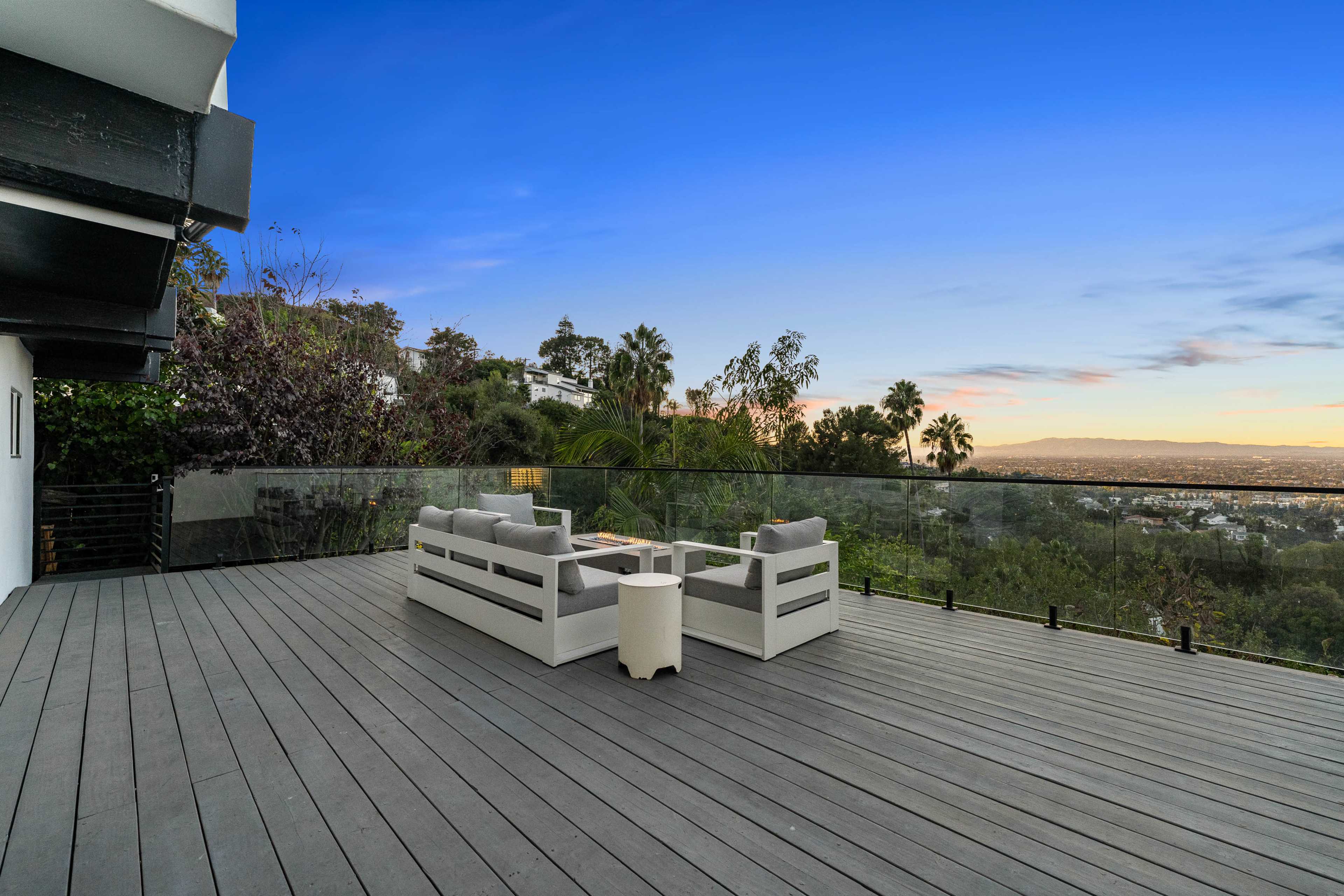 A modern deck features a seating area with a table overlooking a panoramic view of a cityscape and palm trees.