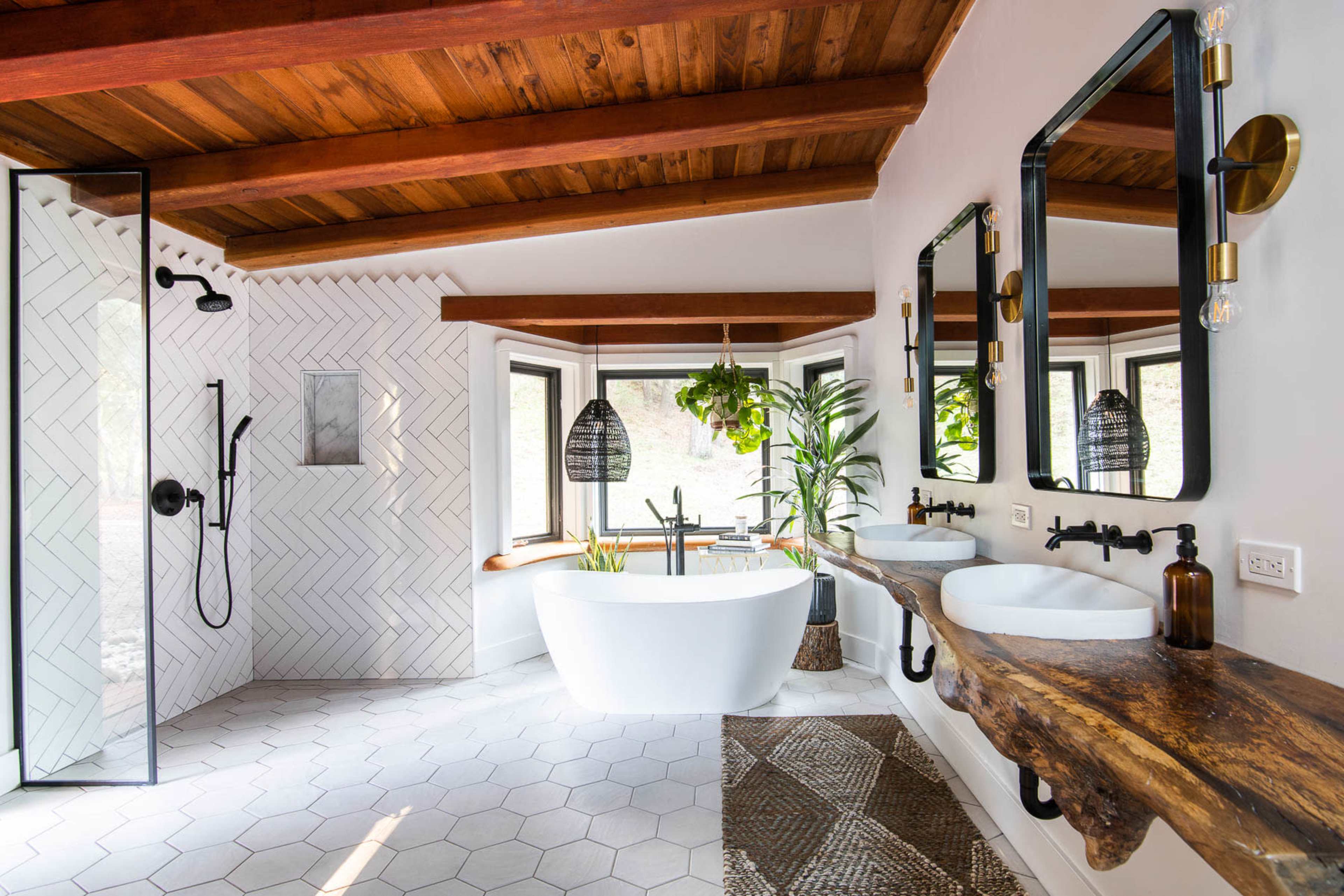 The bathroom features a freestanding white bathtub, dual sinks mounted on a wooden countertop, and a walk-in shower with a glass enclosure, all accented by natural light from multiple windows.