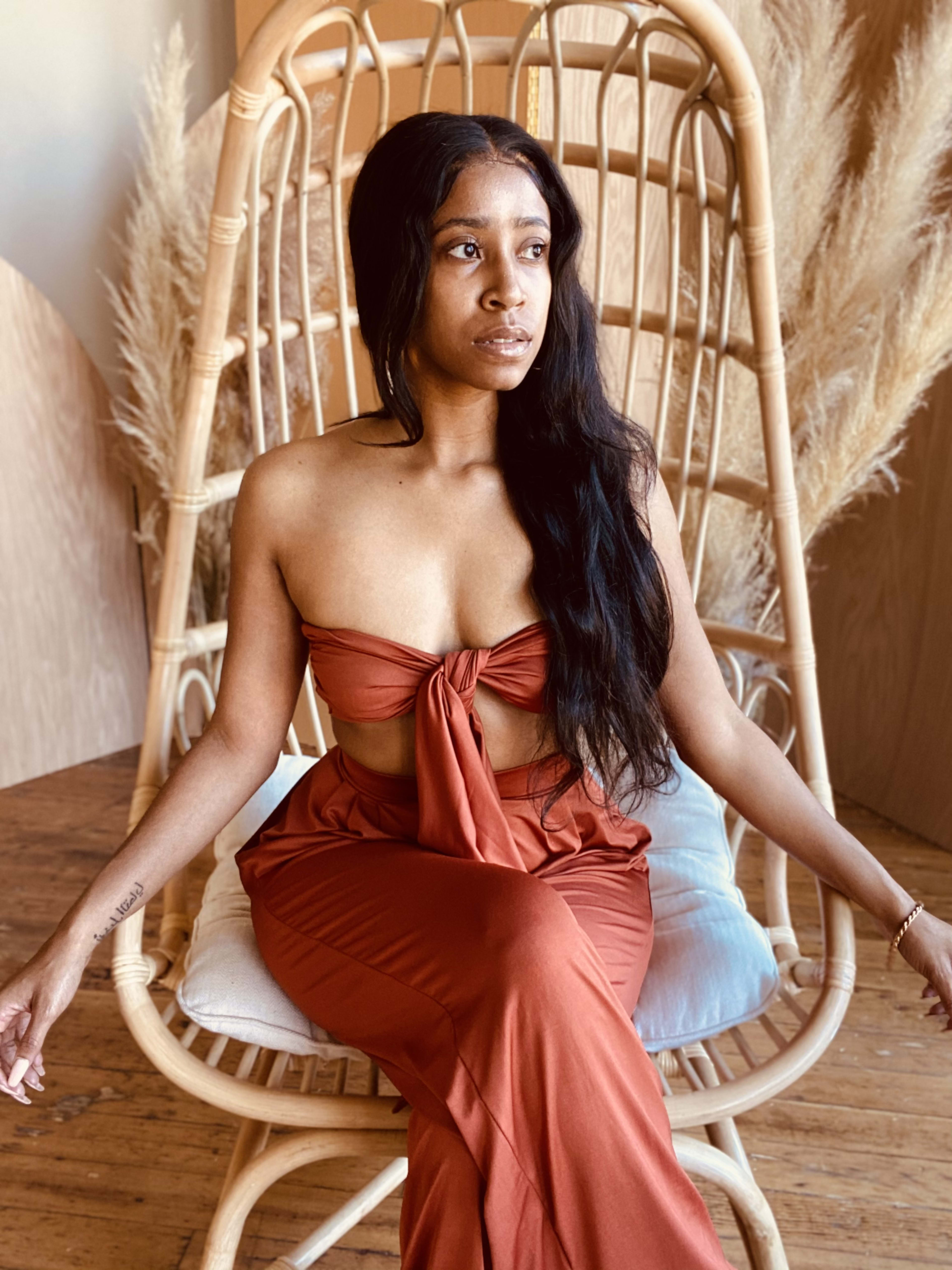 A woman in a red dress posing on a boho wicker chair.