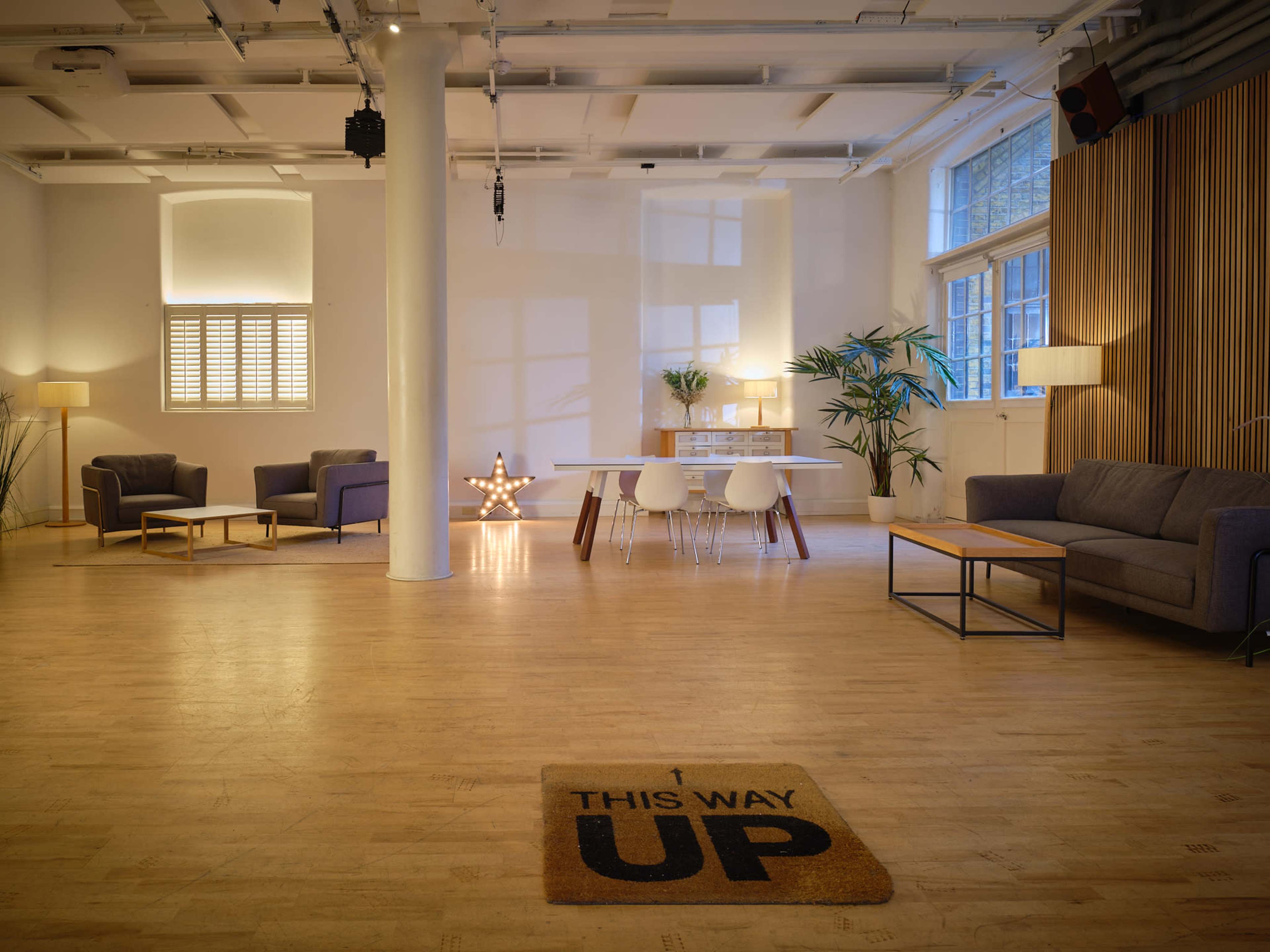 A spacious, well-lit interior with a dining area, seating arrangement, and decorative elements, including a star-shaped light and a welcome mat that reads "THIS WAY UP."