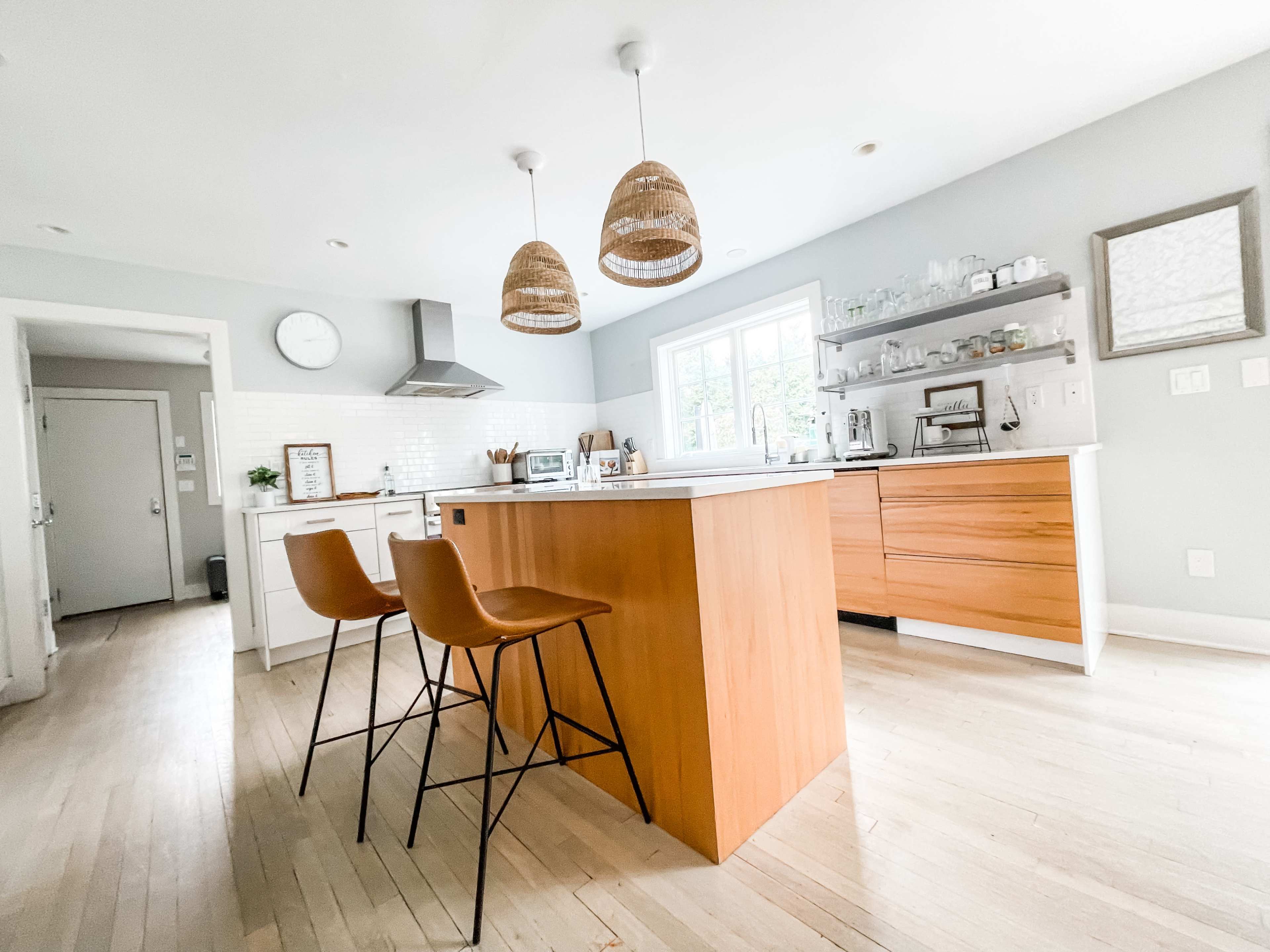 A modern kitchen features a central island with two bar stools, pendant lighting, and sleek cabinetry.