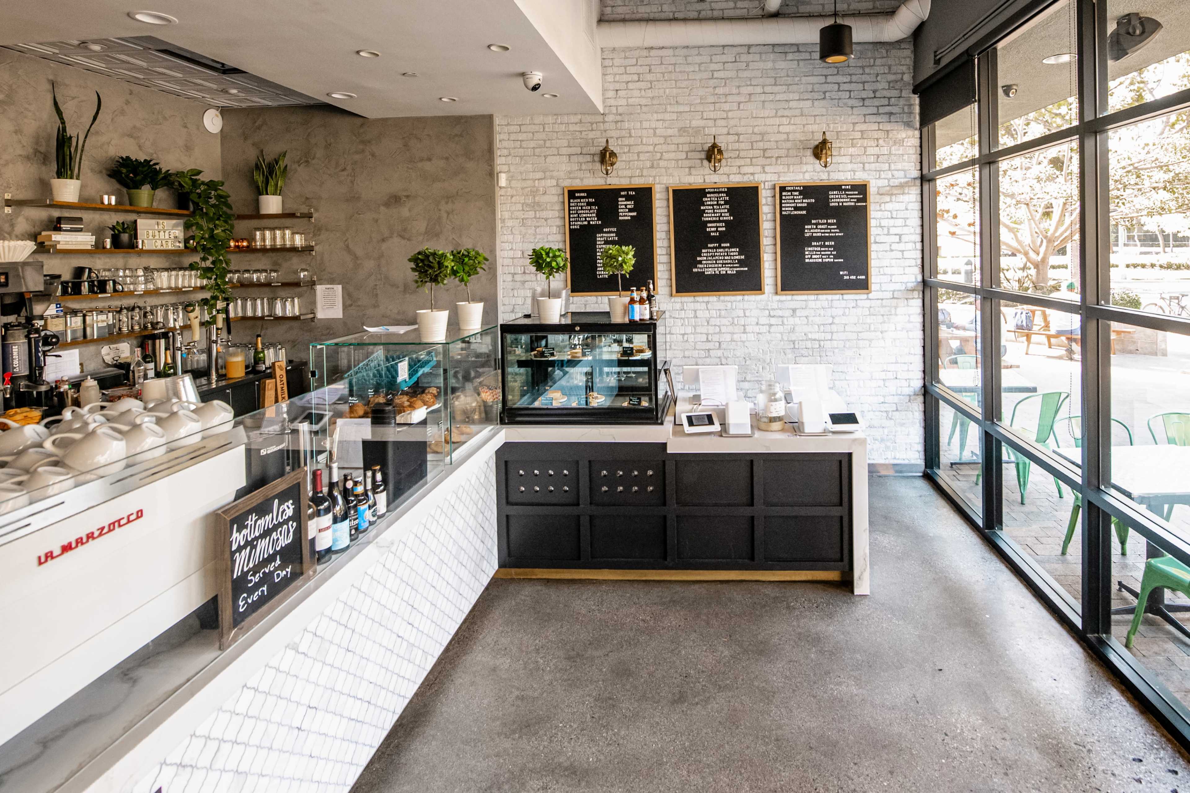 A modern café interior with a service counter displaying pastries and drinks, alongside a menu board on the wall.