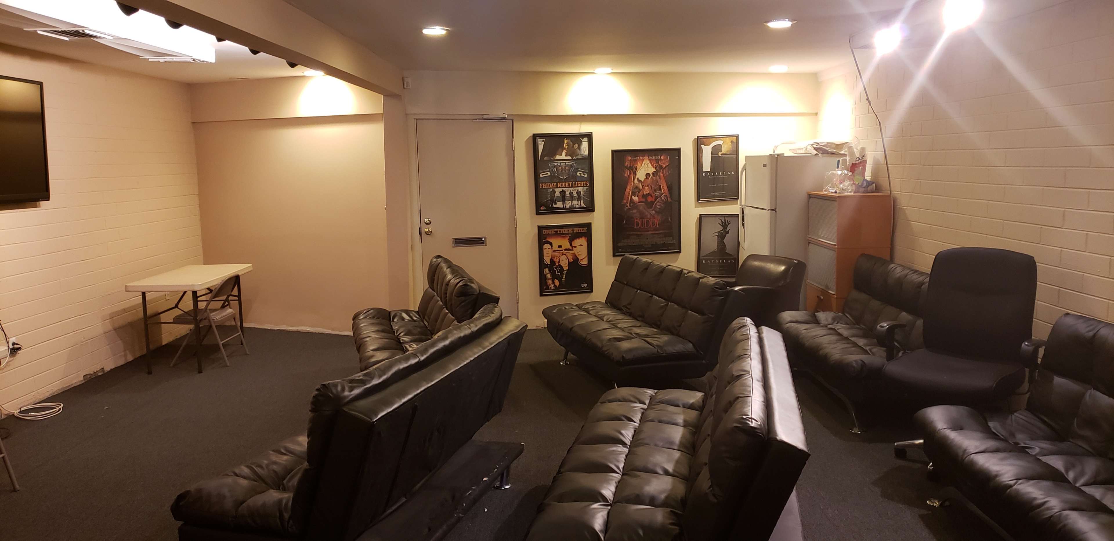 A dimly lit room with several black leather sofas arranged in a circular formation, a small table, and posters on the walls.