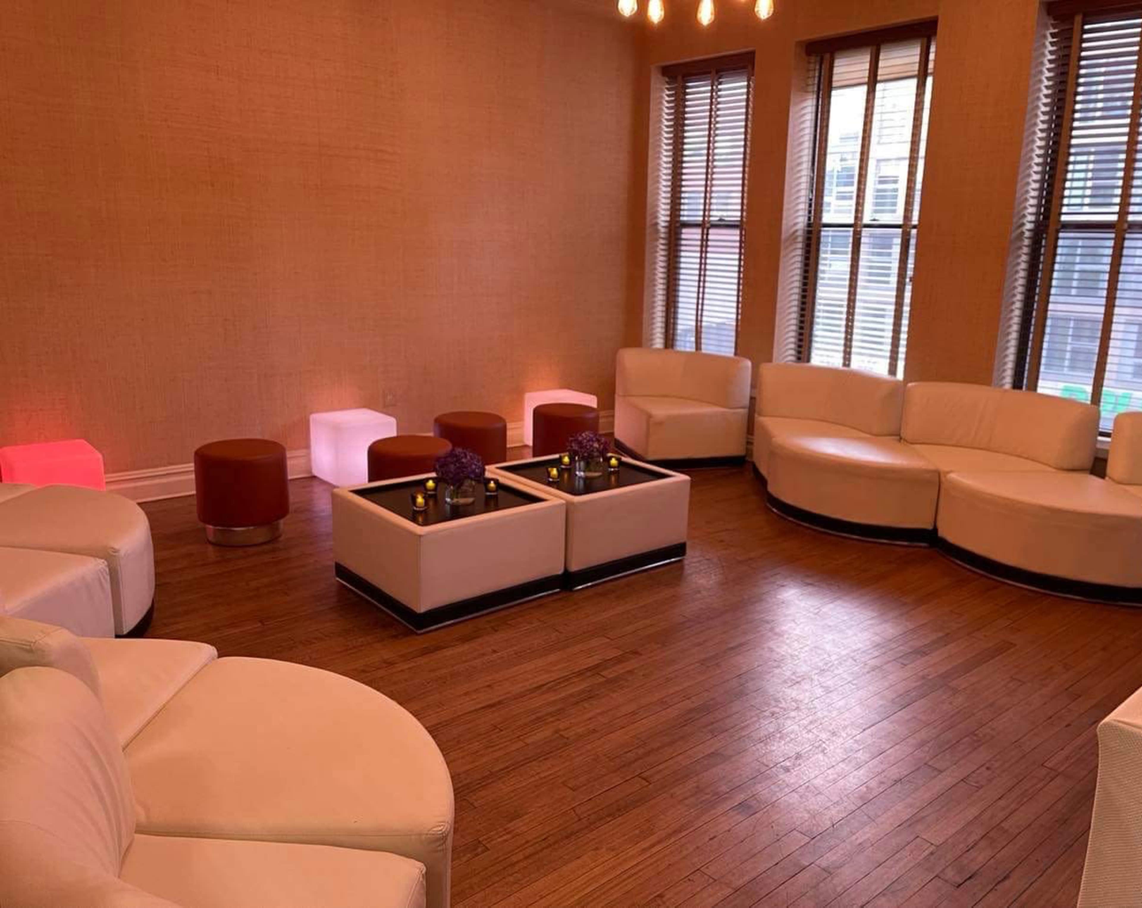 The room features a series of curved white sofas and small tables, arranged around two coffee tables, with large windows allowing natural light to enter.