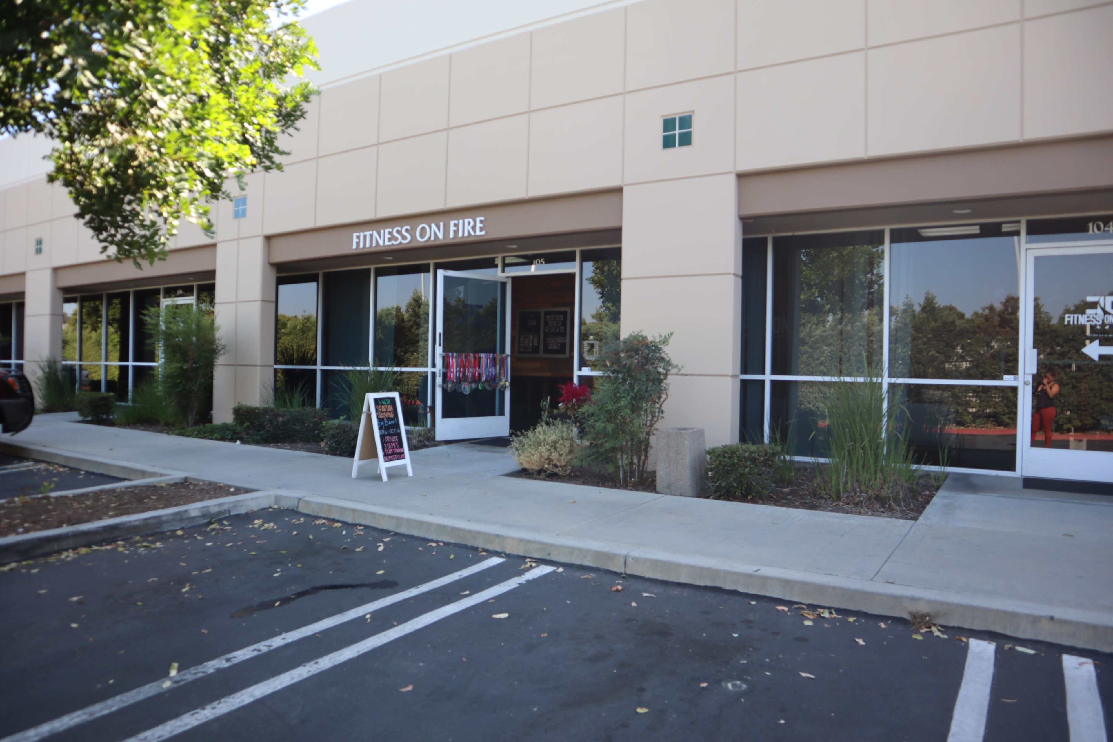The exterior of a fitness studio named "Fitness on Fire" is shown, featuring a storefront with large windows and a sidewalk sign.