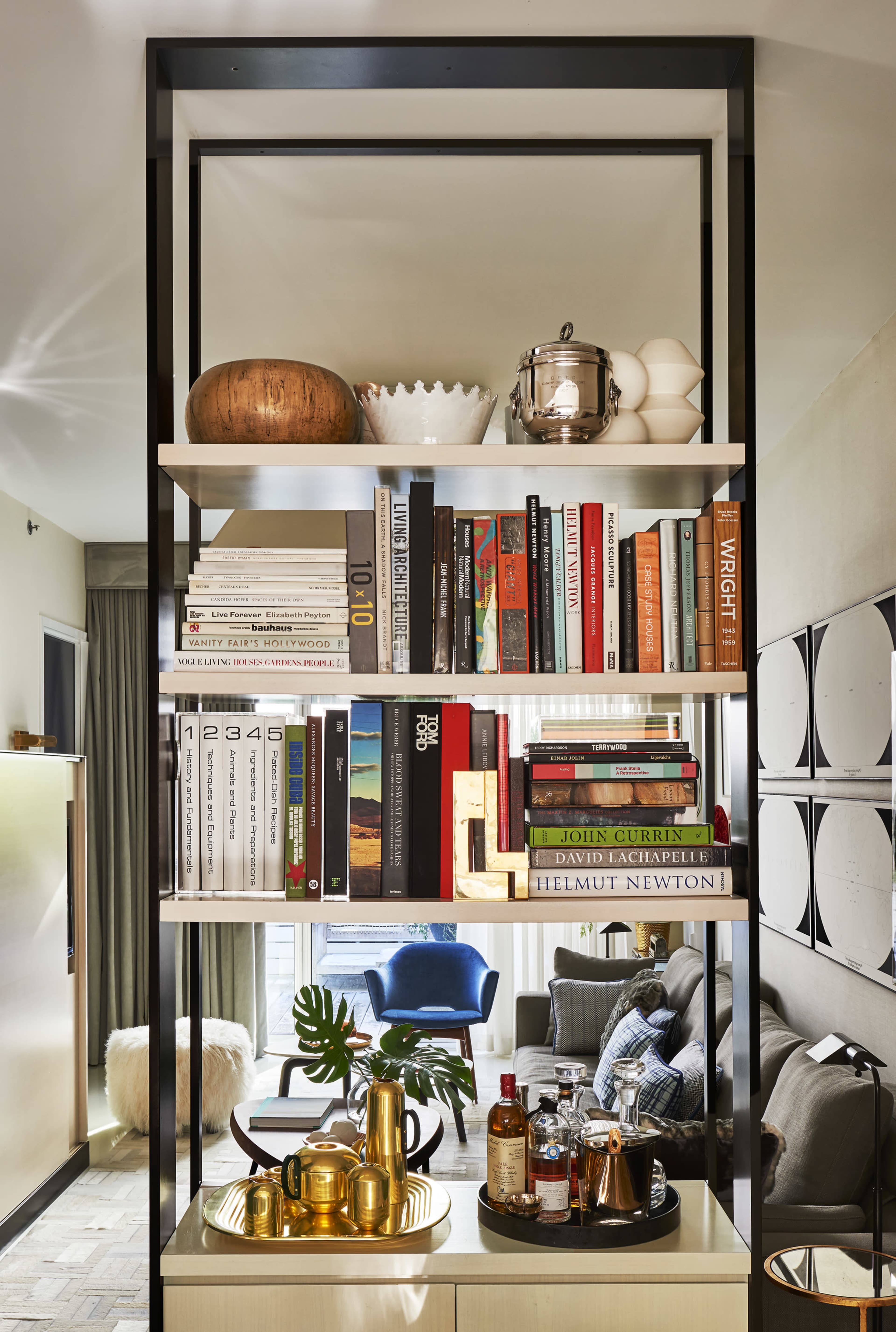 A modern open shelving unit filled with books, decorative objects, and a minimalist arrangement, set against a backdrop of a well-furnished living area.
