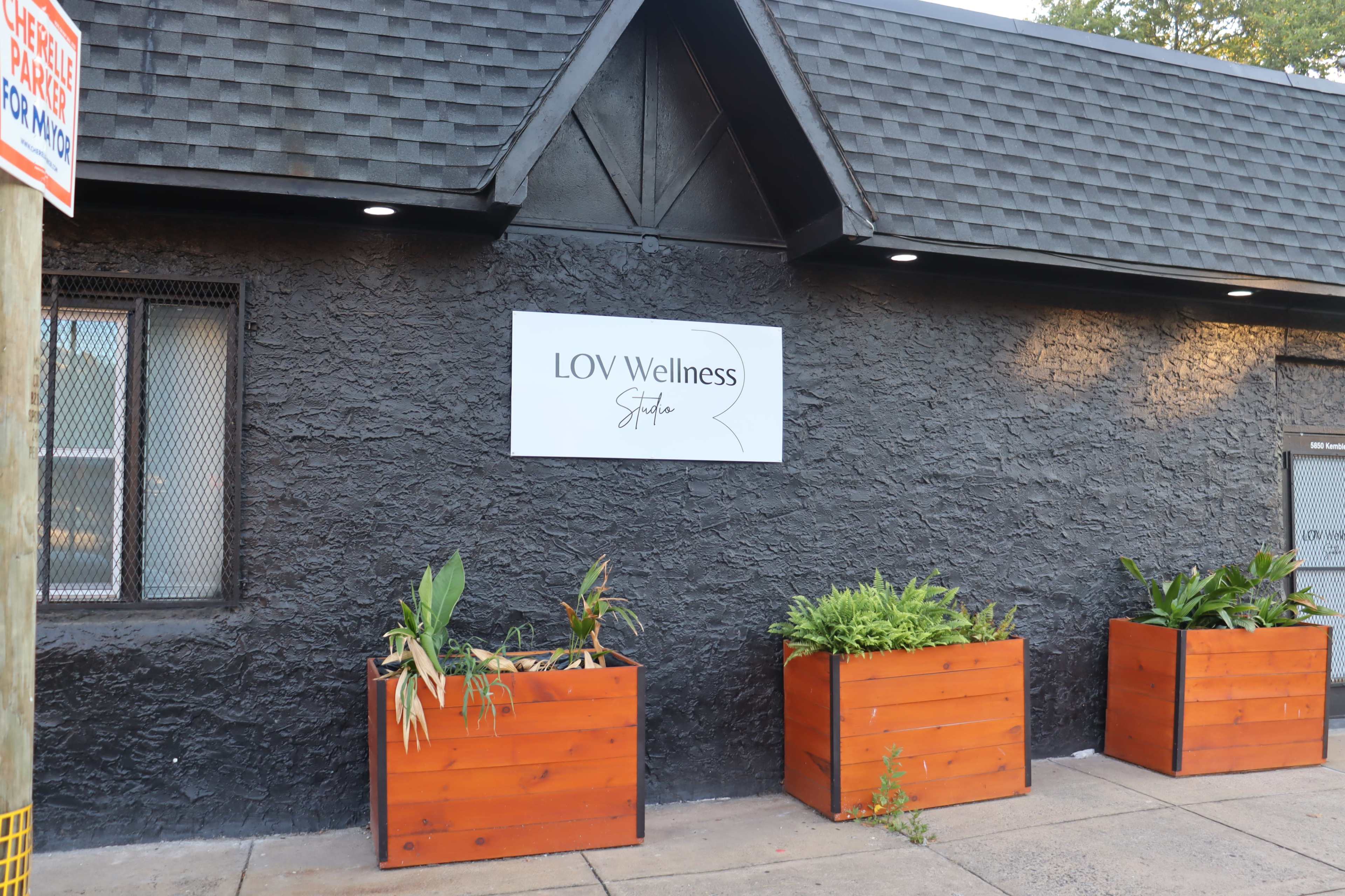 The exterior of a building features a sign reading "LOV Wellness" and several wooden planters with plants.