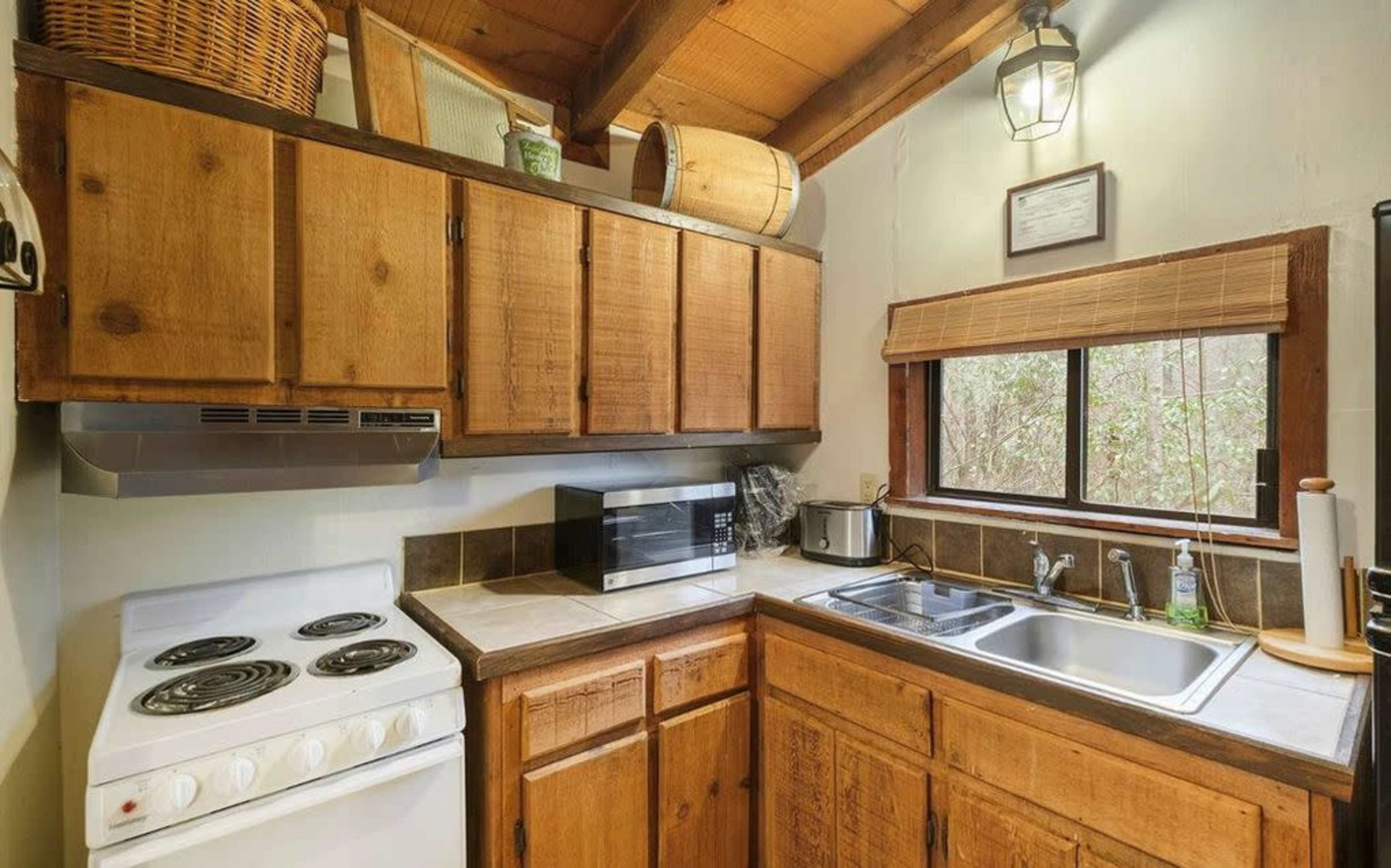 A compact kitchen featuring wooden cabinets, a stove, a microwave, and a window providing natural light.