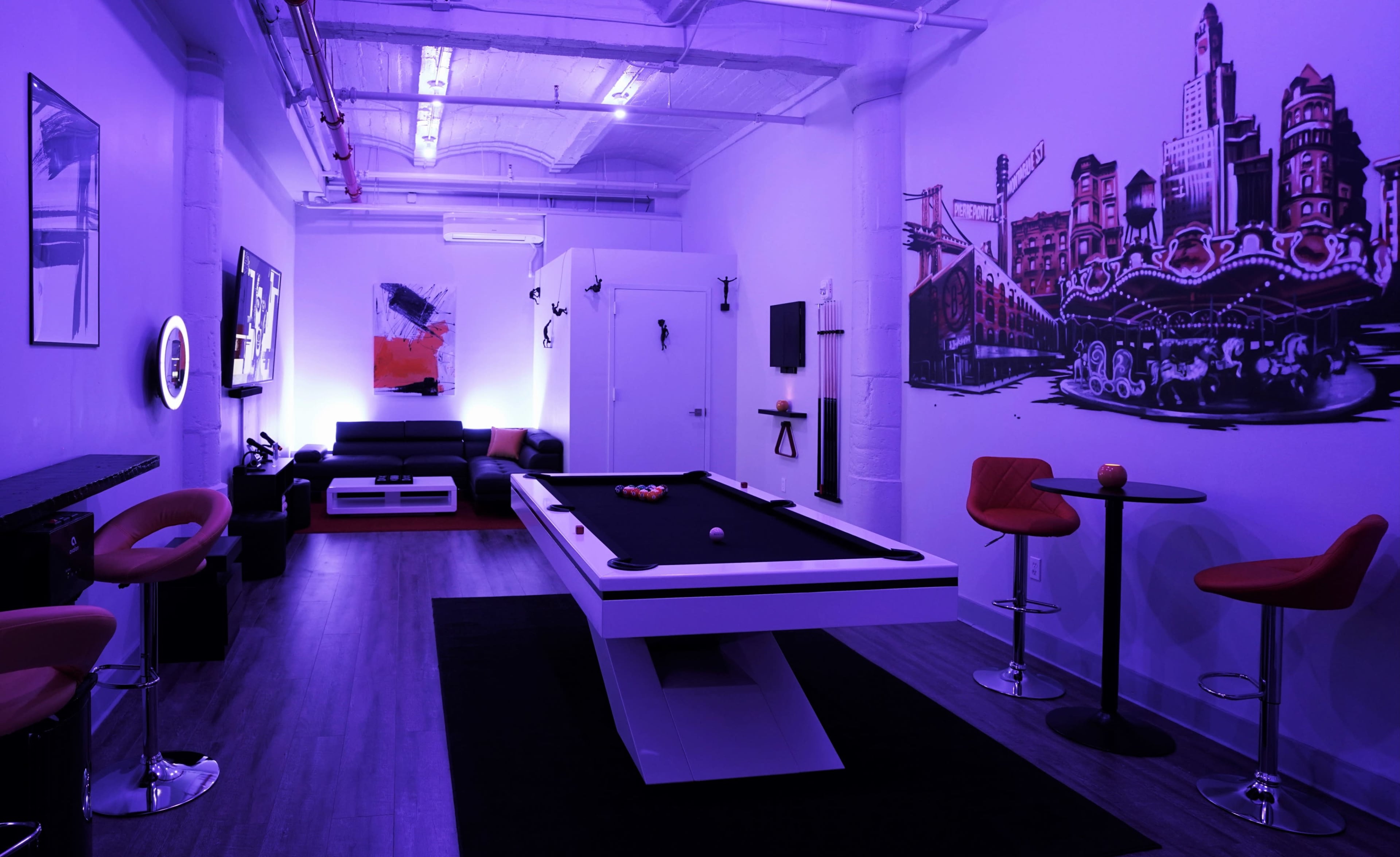 The room features a pool table in the center, surrounded by modern furniture, illuminated by purple lighting and adorned with a mural on the wall.