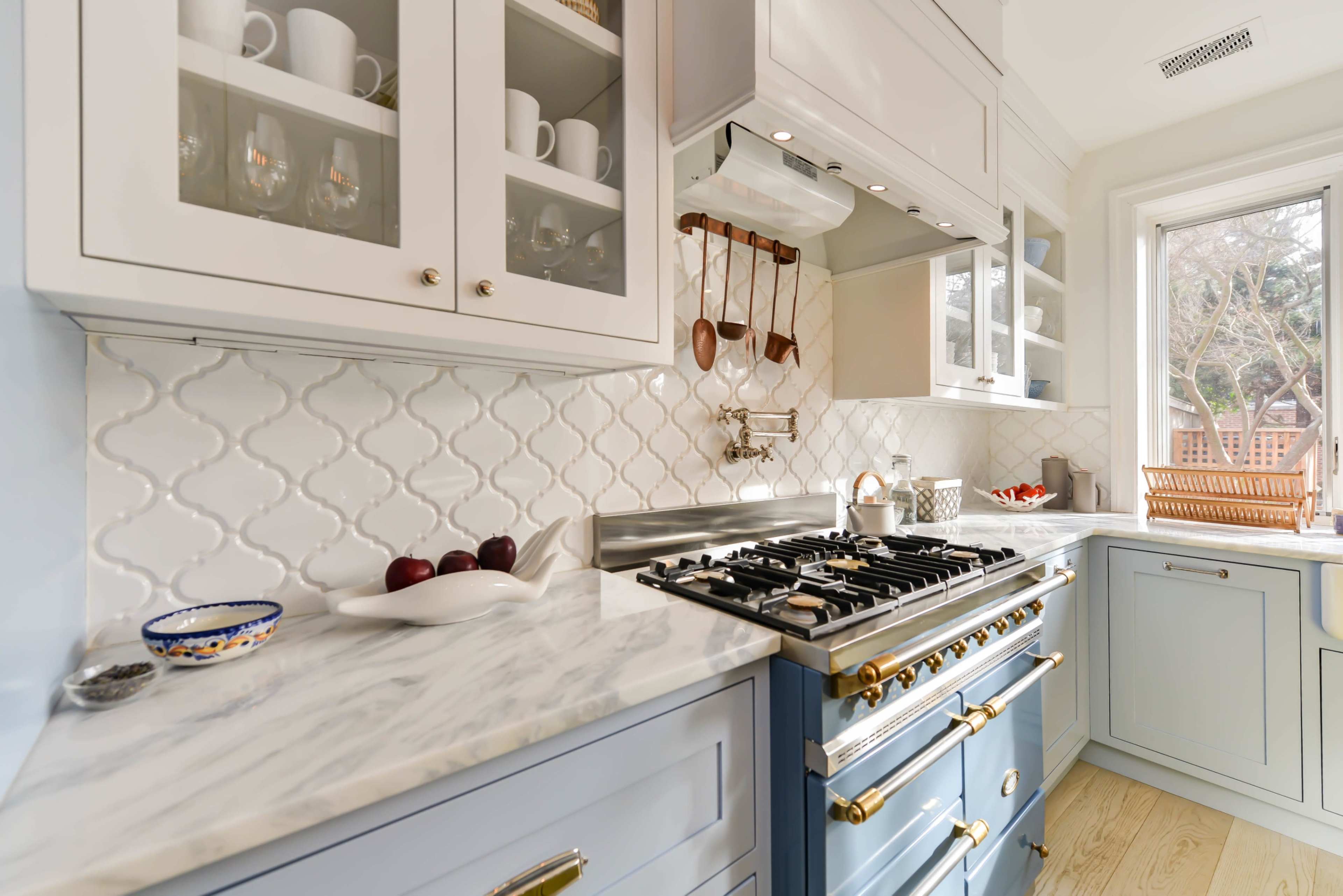 A modern kitchen featuring blue cabinetry, a marble countertop, and a stainless steel stove under a range hood.