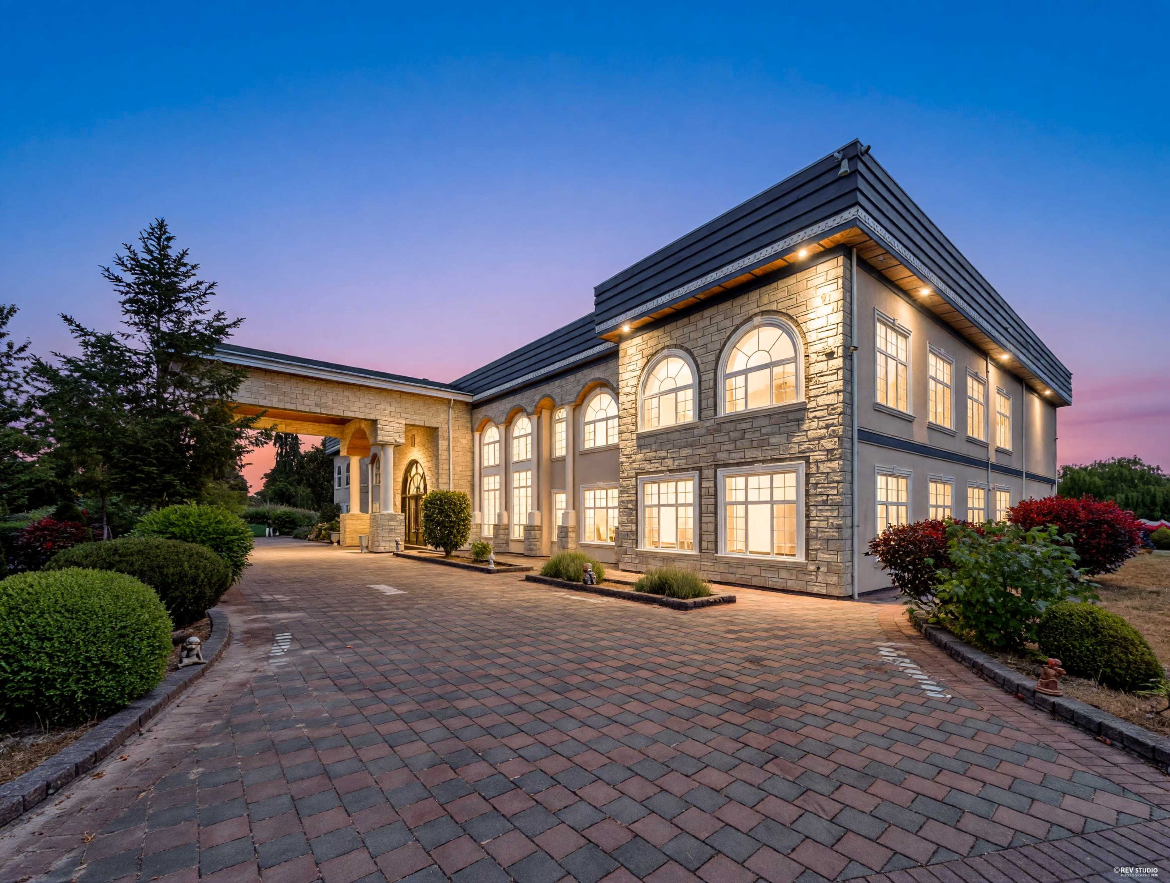 The image shows a large, modern building with a stone facade and large arched windows, set against a twilight sky.
