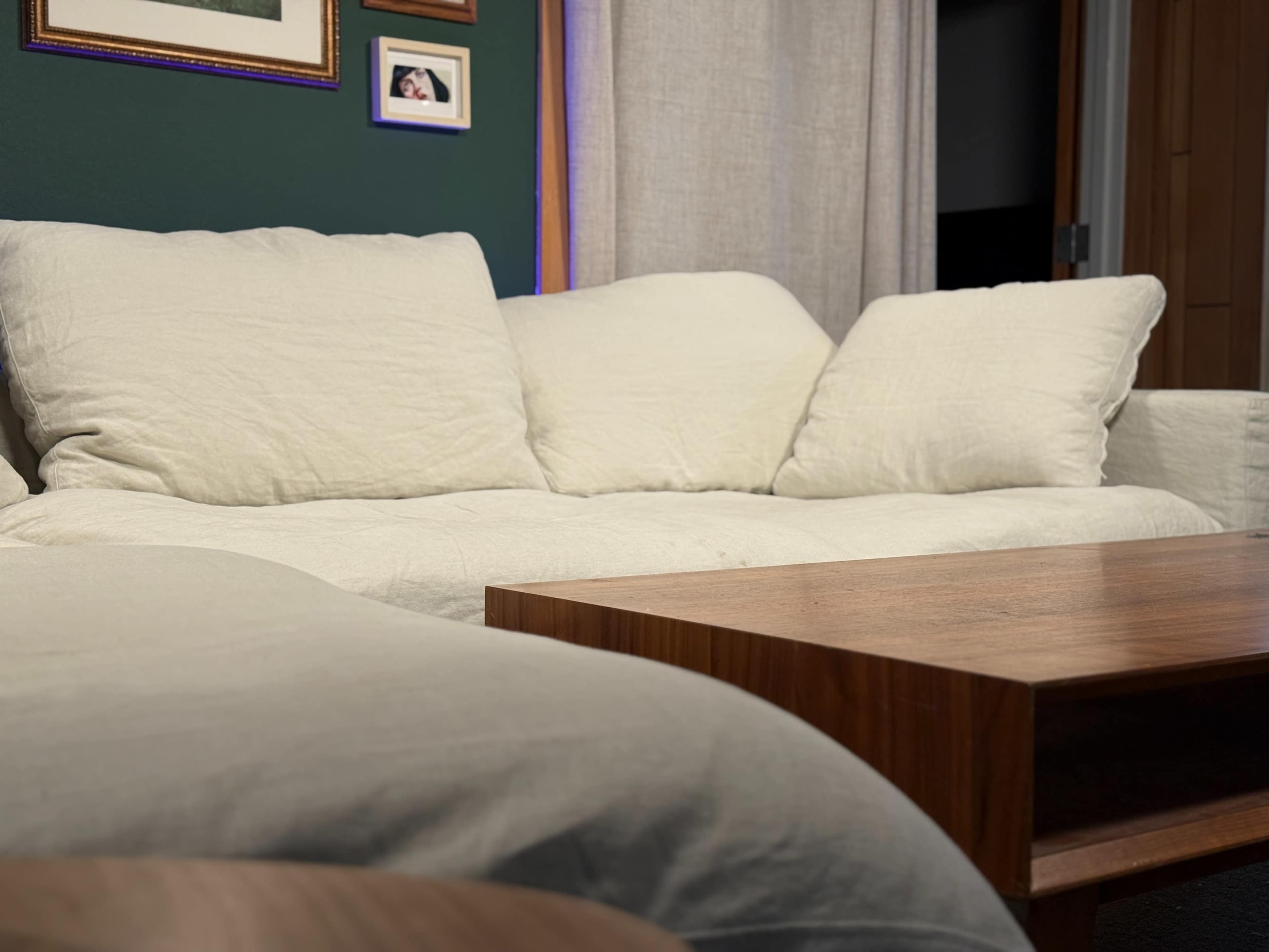A light-colored couch sits in a room with green walls and framed pictures on the wall behind it, accompanied by a wooden coffee table.