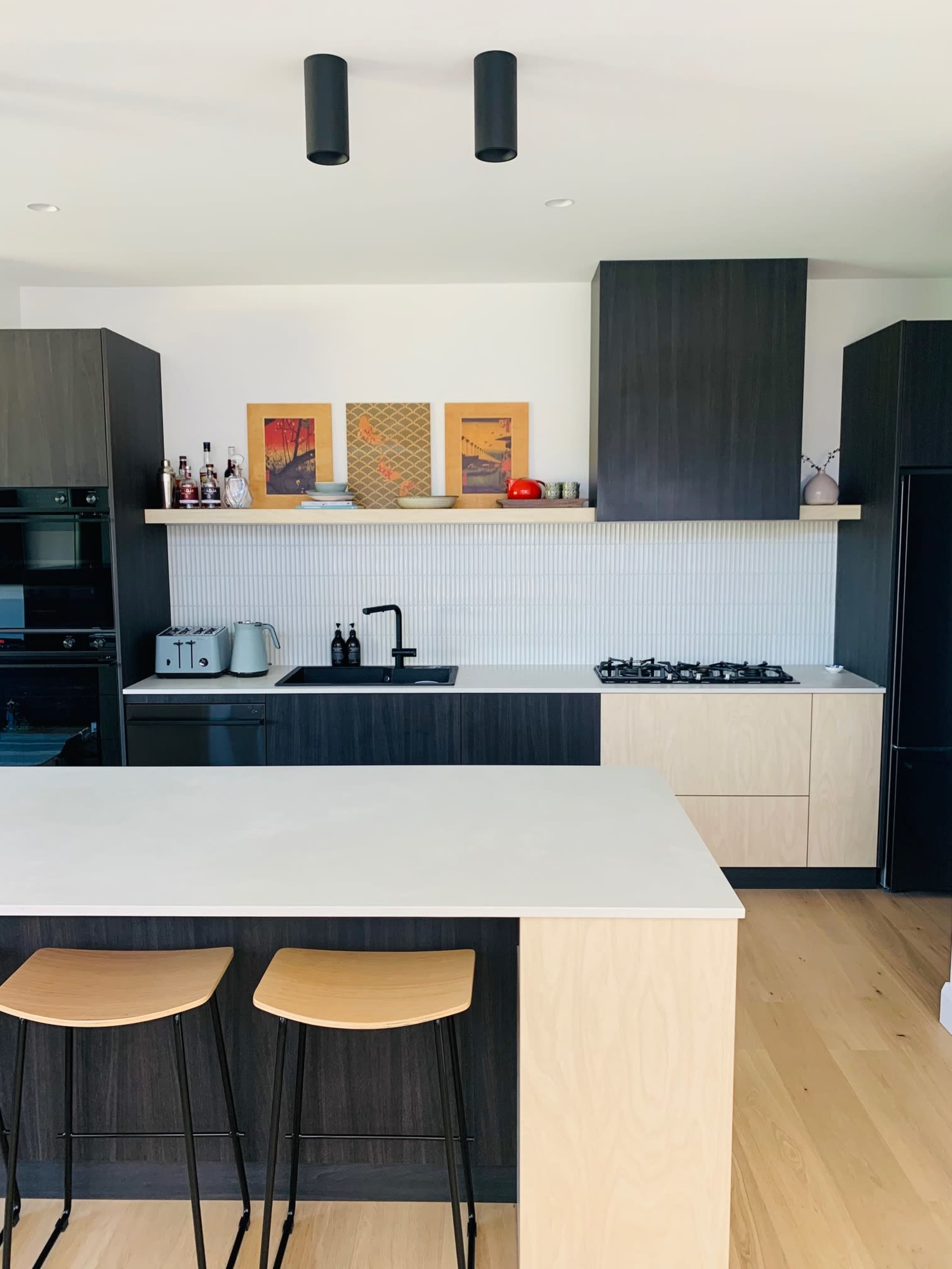 A modern kitchen features dark cabinetry, a light-colored countertop, and two wooden bar stools at an island.