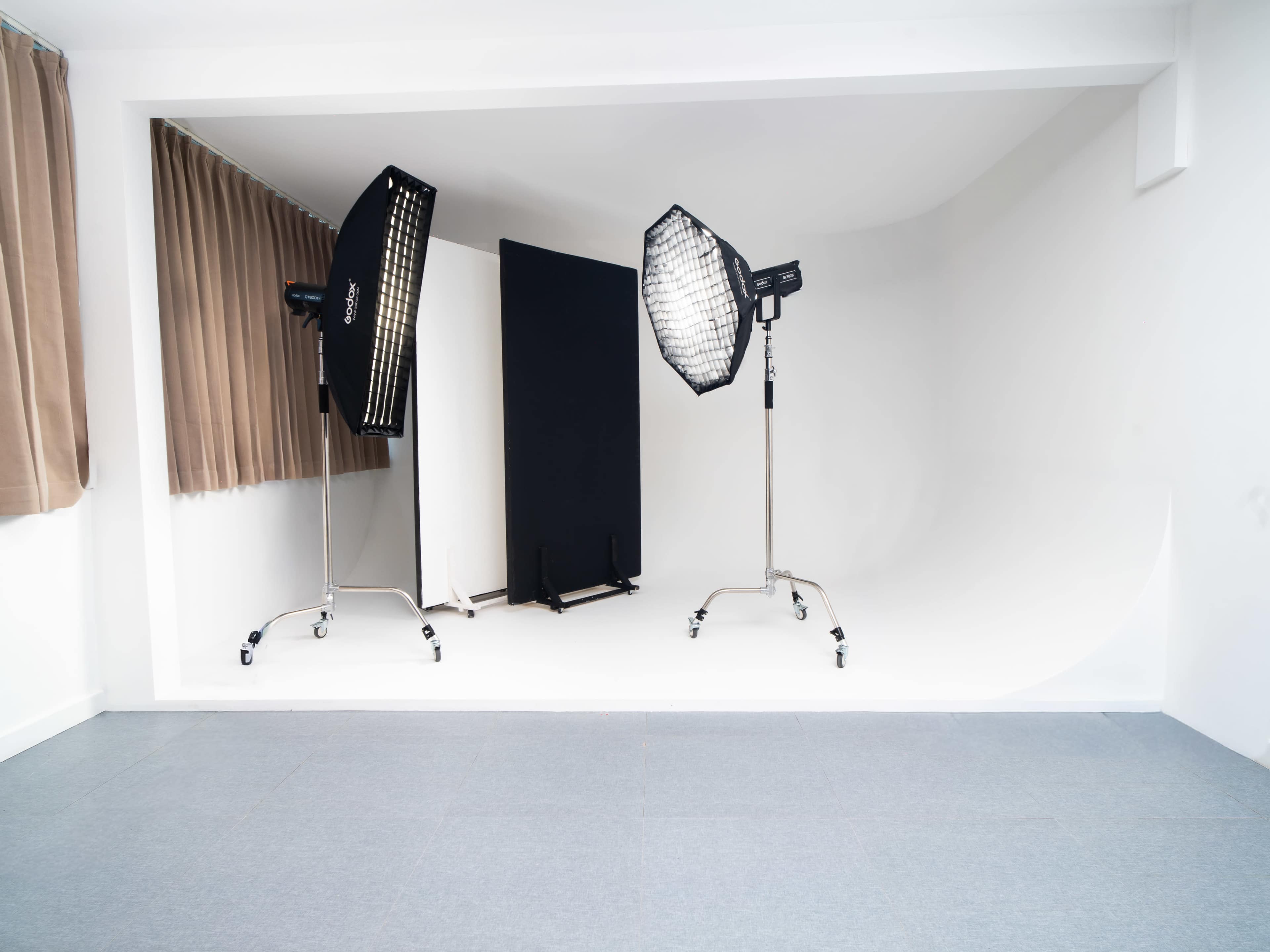 The image shows a photography studio with two lighting setups and a large backdrop against a white wall.