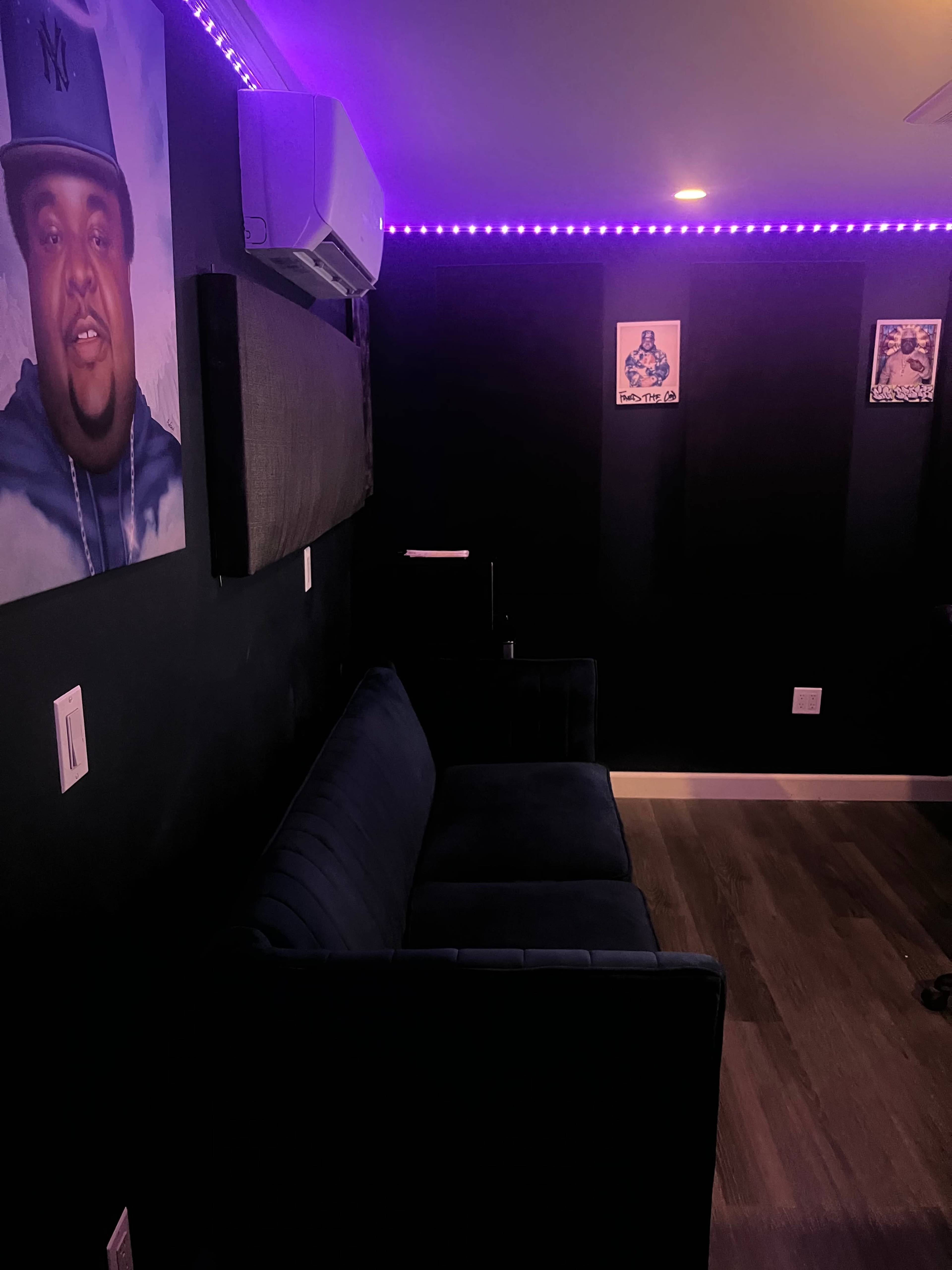 A dimly lit room featuring a dark wall with a blue couch and purple LED strip lighting.