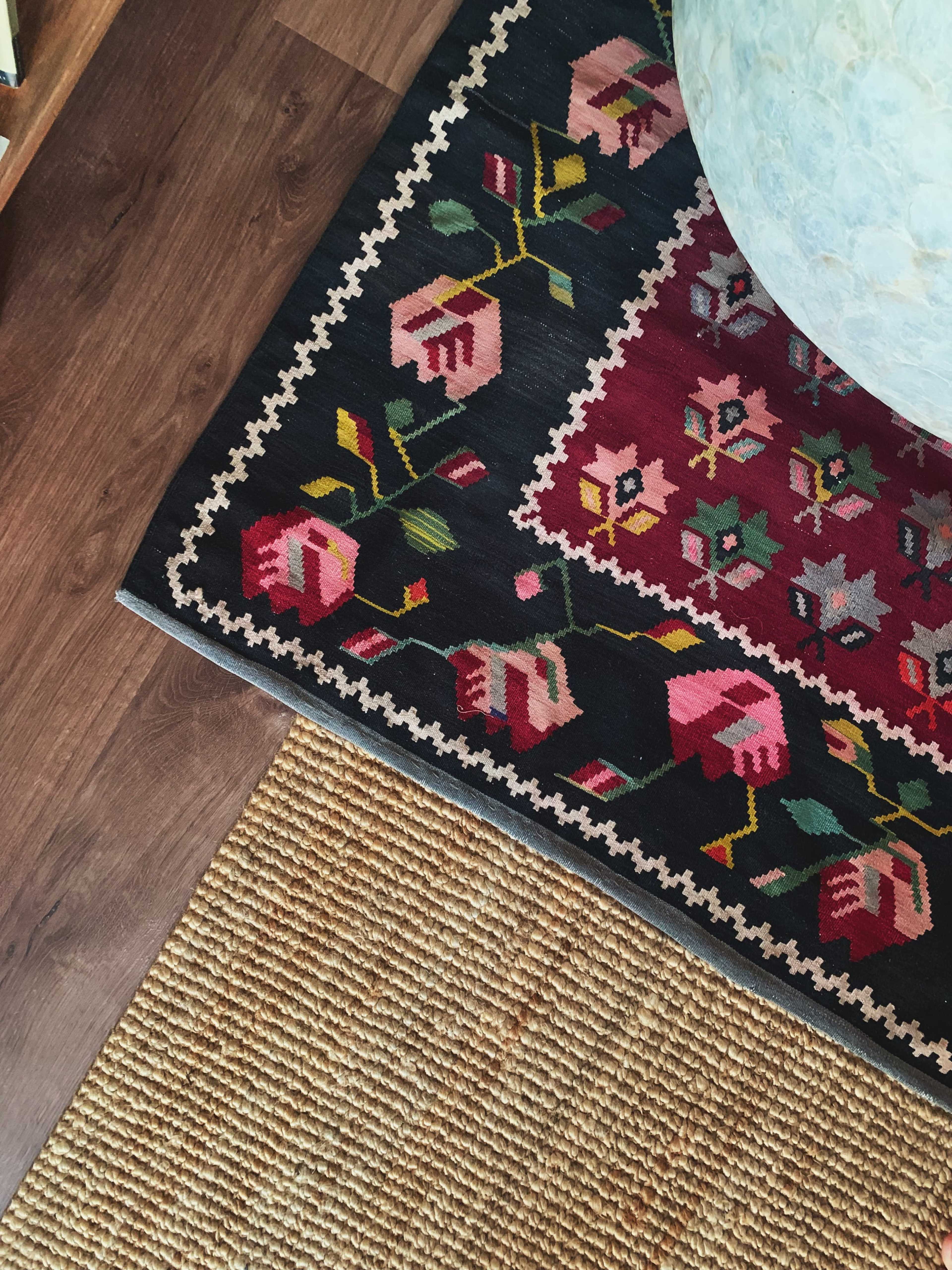 The image shows a corner of a floor featuring a patterned rug with floral designs, positioned next to a jute rug on a wooden surface.