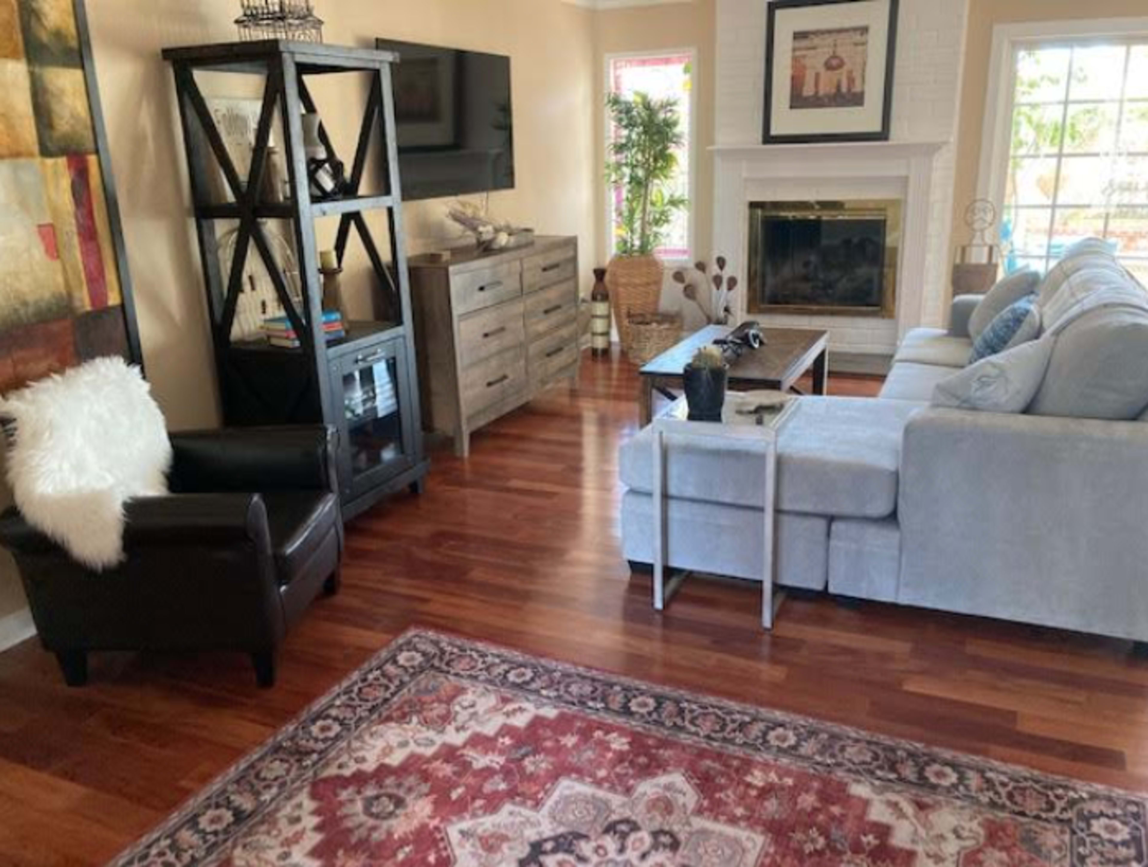 A living room with wooden floors, a gray sectional sofa, a coffee table, and various furniture pieces including a television stand and a dresser.