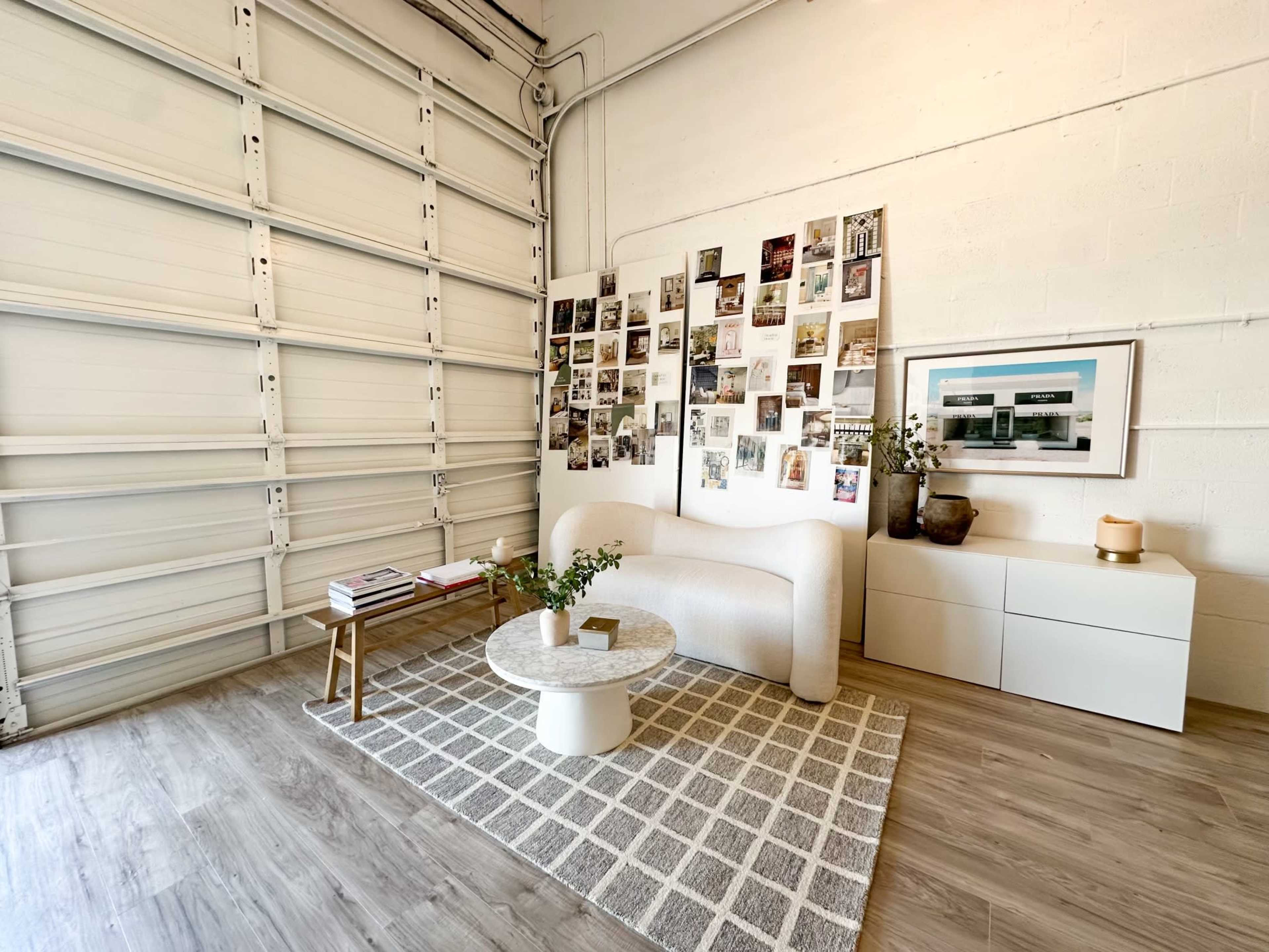 A minimalist living space features a curved white sofa, a marble-top coffee table, and a wall adorned with a collage of photos.