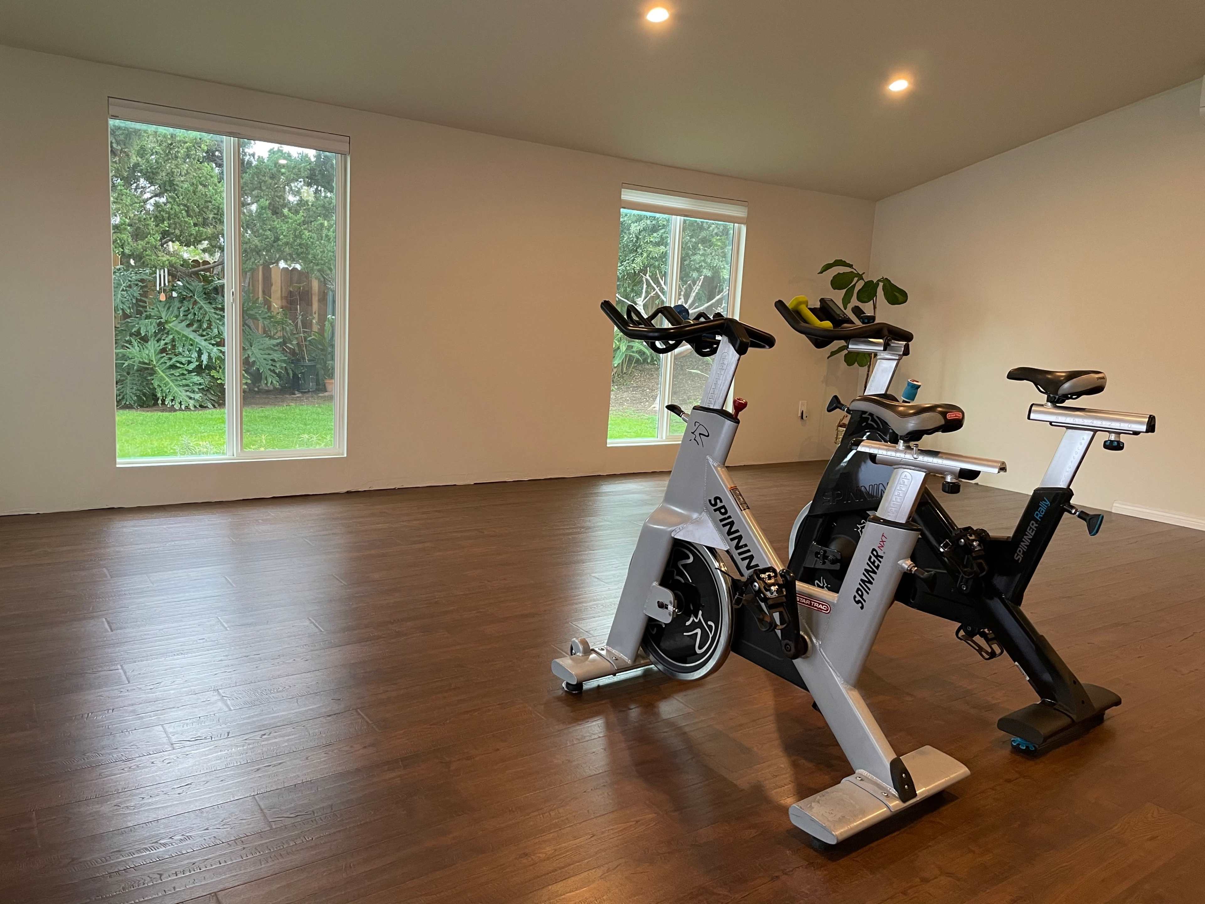 Two stationary exercise bikes positioned in a spacious room with large windows overlooking a green landscape.